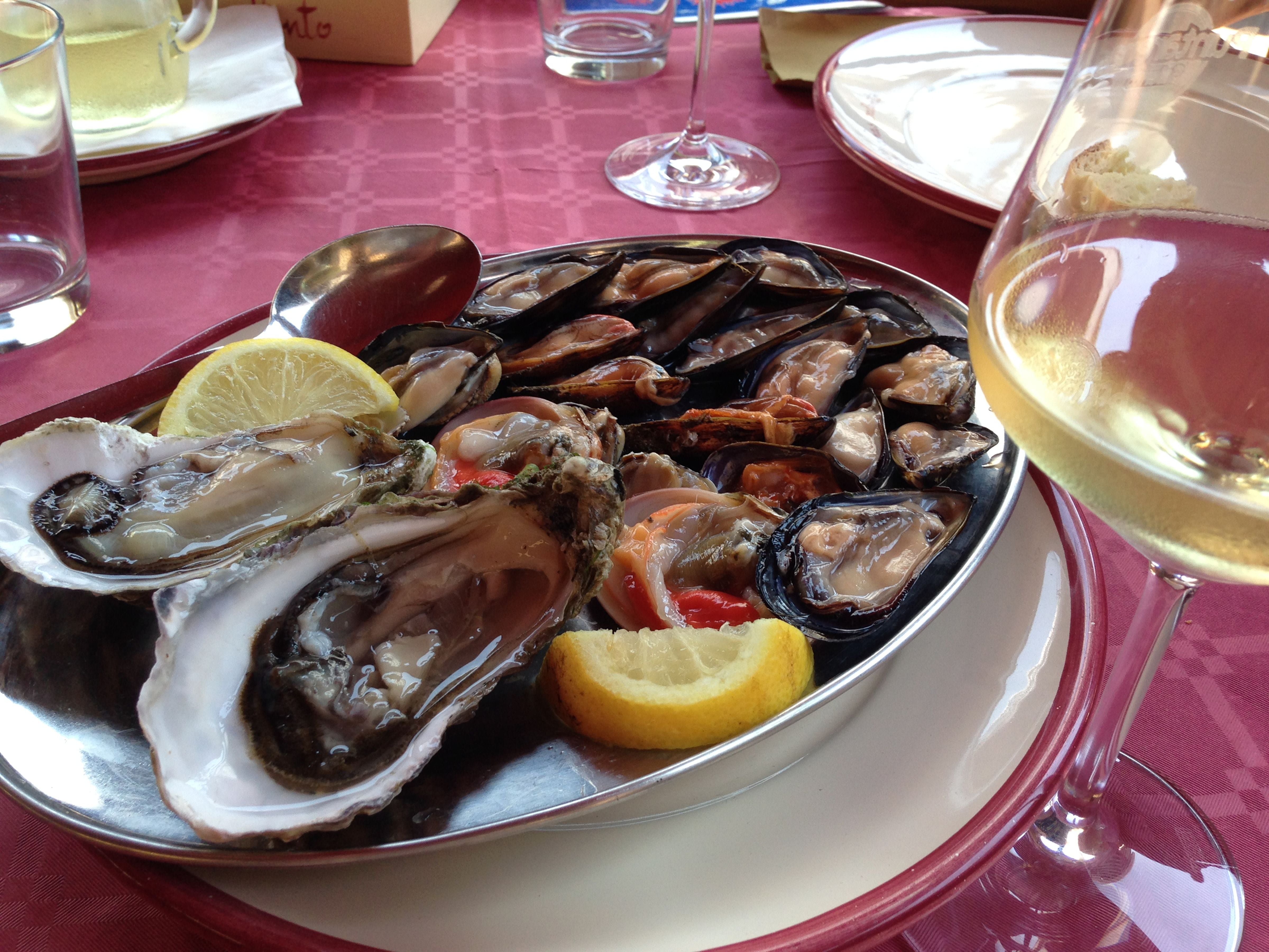 Teller mit Muscheln und Austern, Zitronenscheiben und ein Glas Weißwein auf einem Restauranttisch.