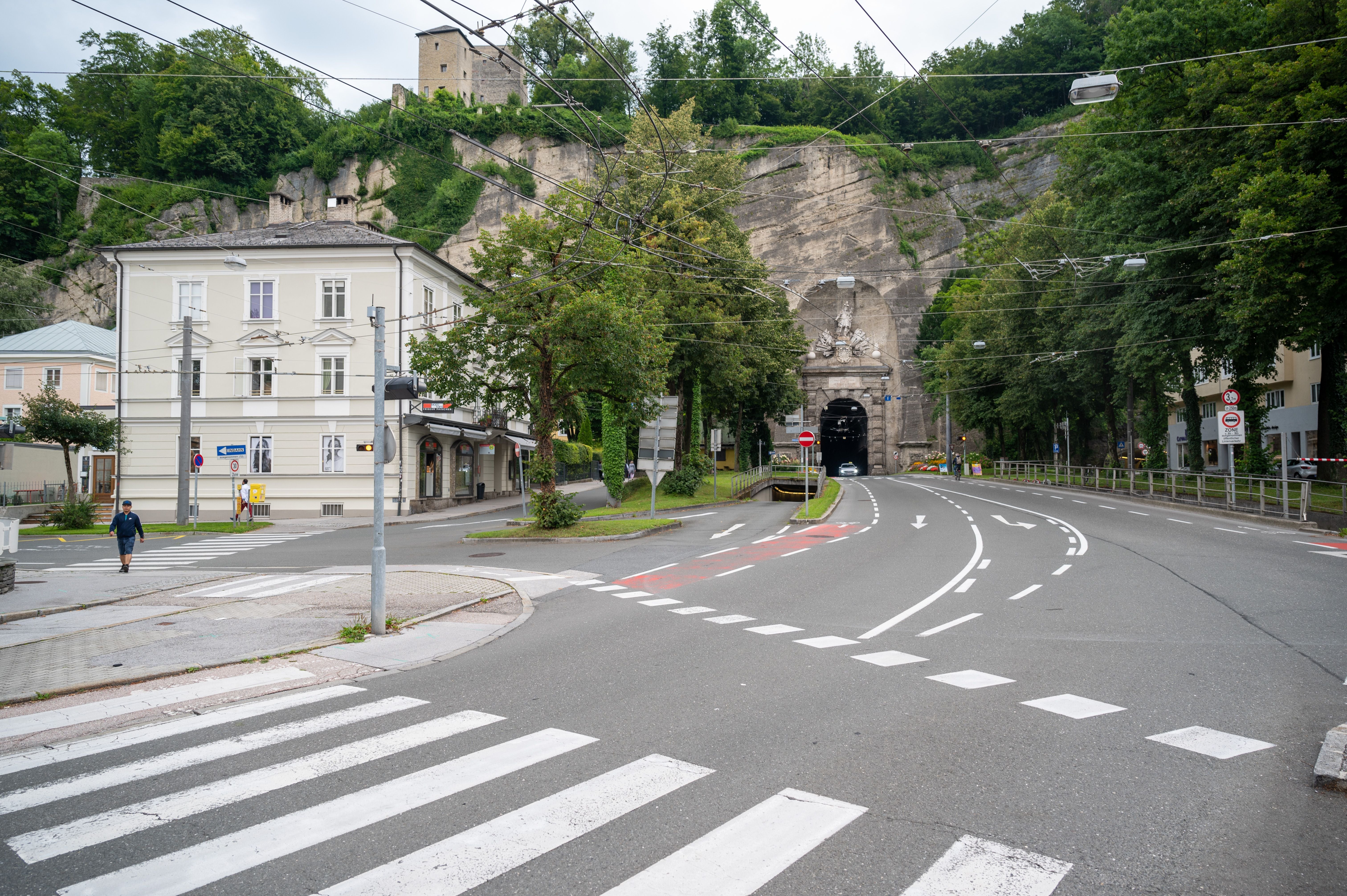 Leere Straßenkreuzung mit Straßentunnel im Hintergrund und wenigen Fußgängern in einer Stadt.