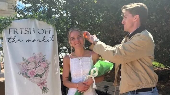 Junger Mann steckt einer lächelnden Frau mit Blumenstrauß eine Blume ins Haar.