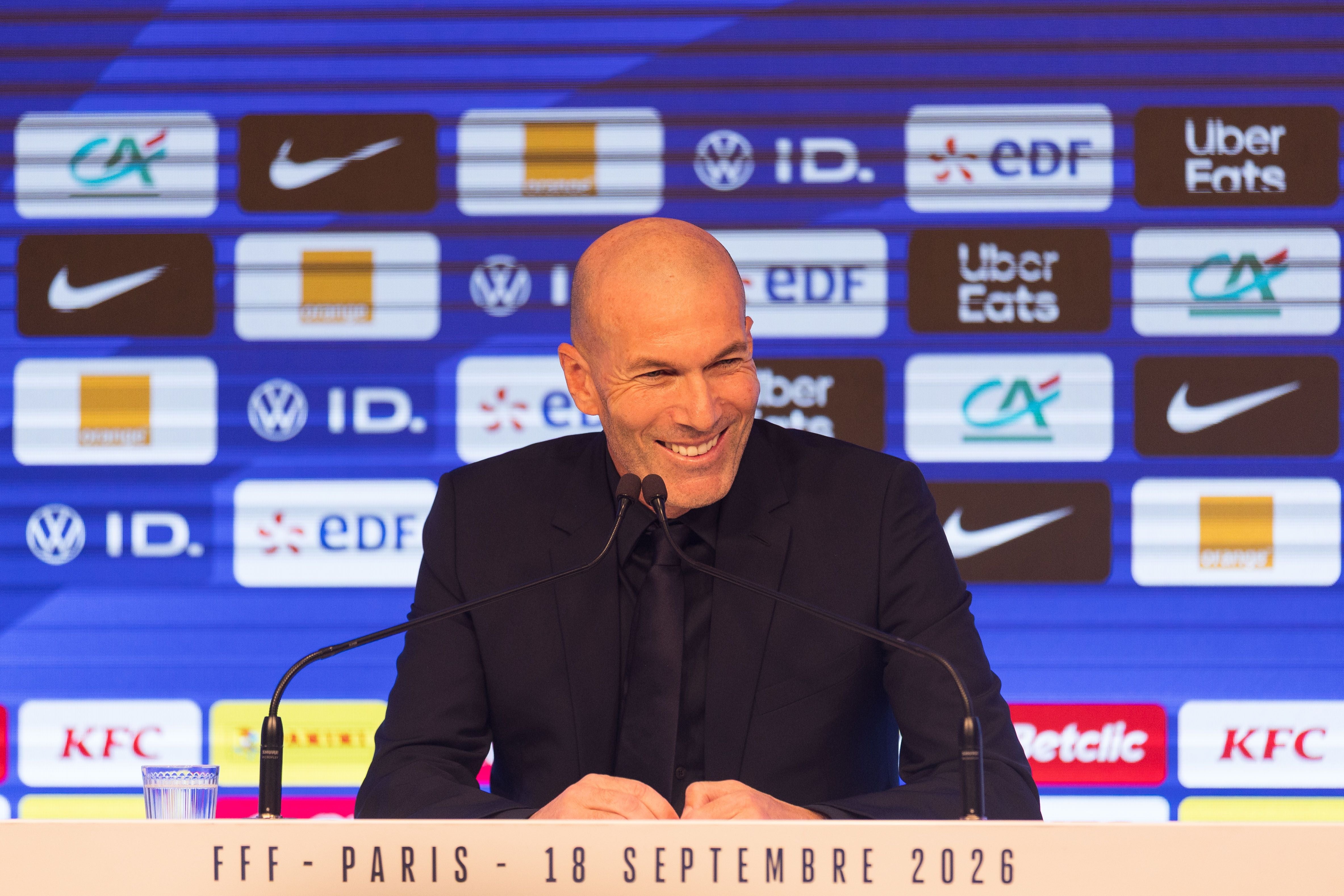 Zinedine Zidane im dunklen Anzug lächelt entspannt bei einer Pressekonferenz des französischen Fußballverbands.