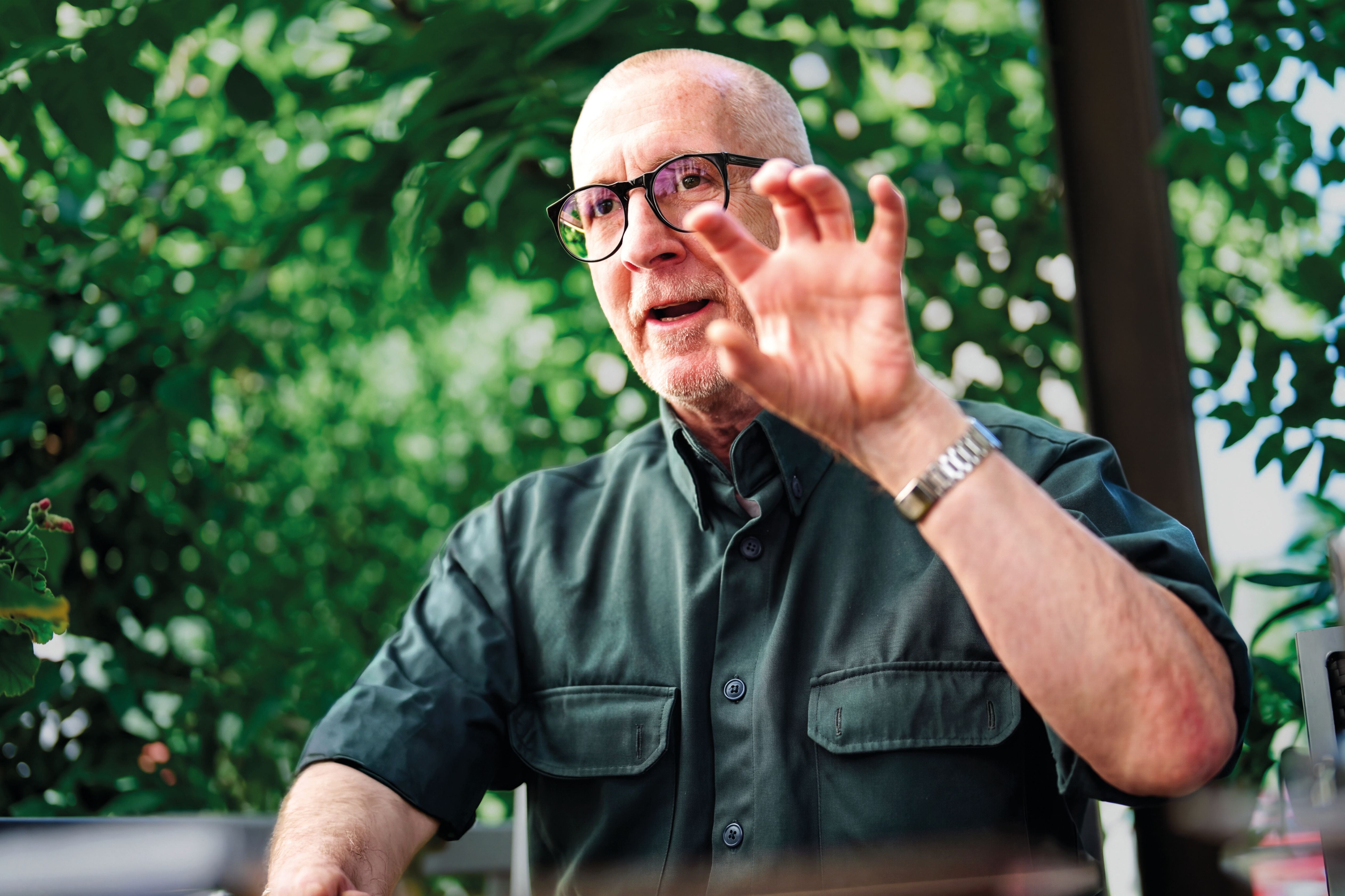 Ein älterer Mann mit Brille und grünem Hemd gestikuliert lebhaft im Grünen.