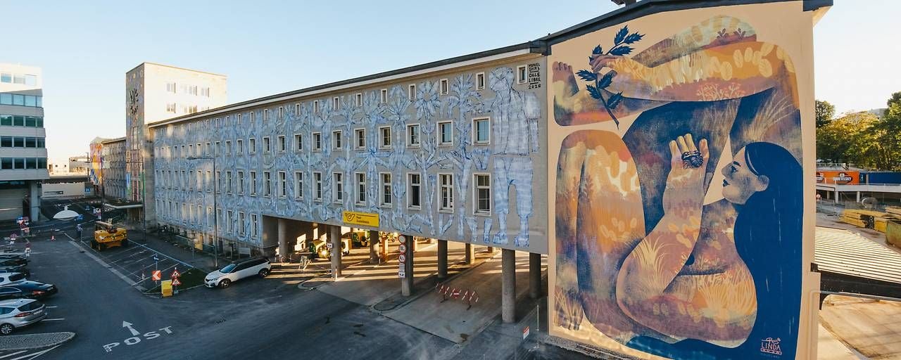 Großes Wandgemälde an einem Gebäude, das eine abstrakte Frau mit Pflanzen zeigt.