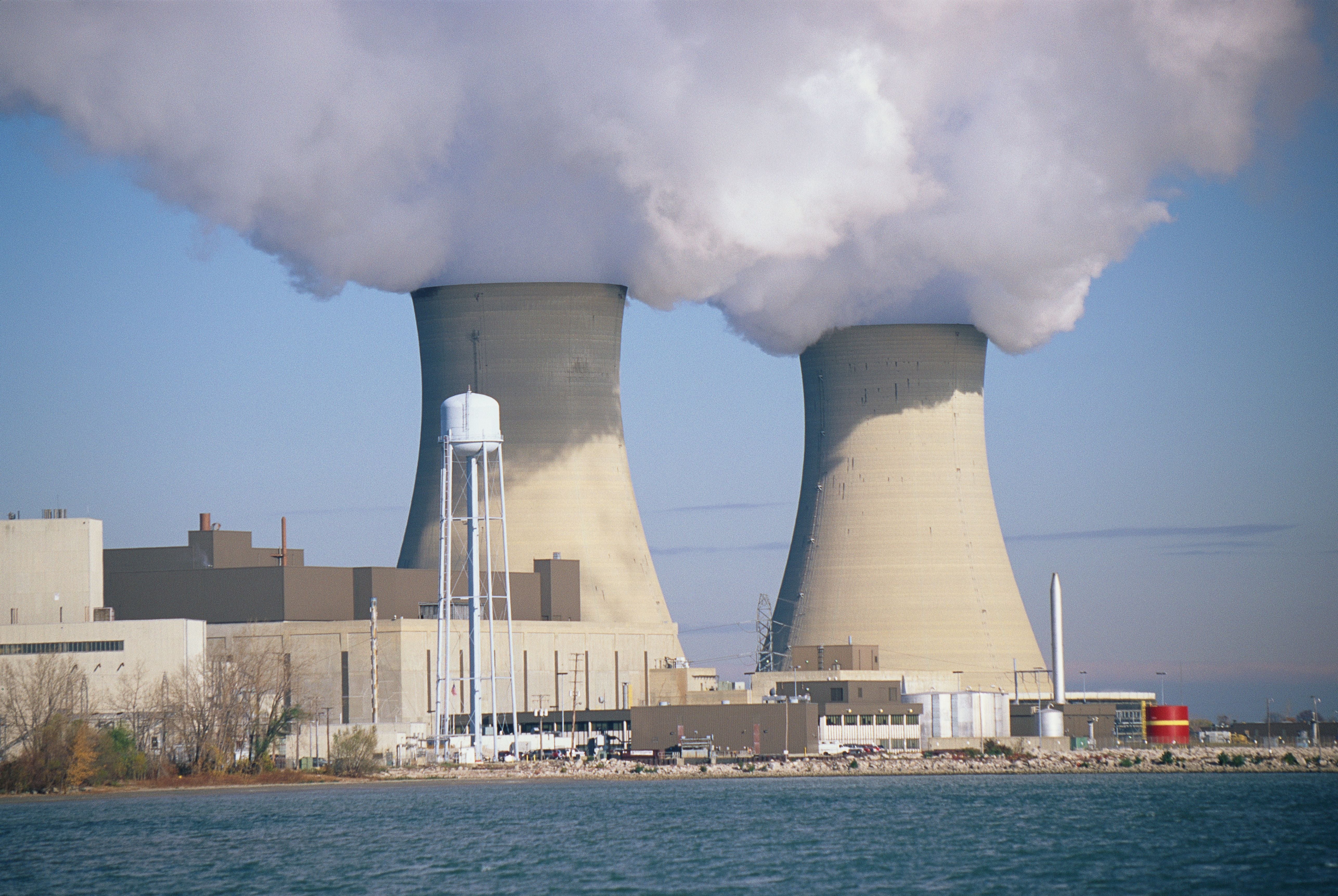Kernkraftwerk mit zwei Kühltürmen, aus denen Dampf aufsteigt, am Wasser gelegen.