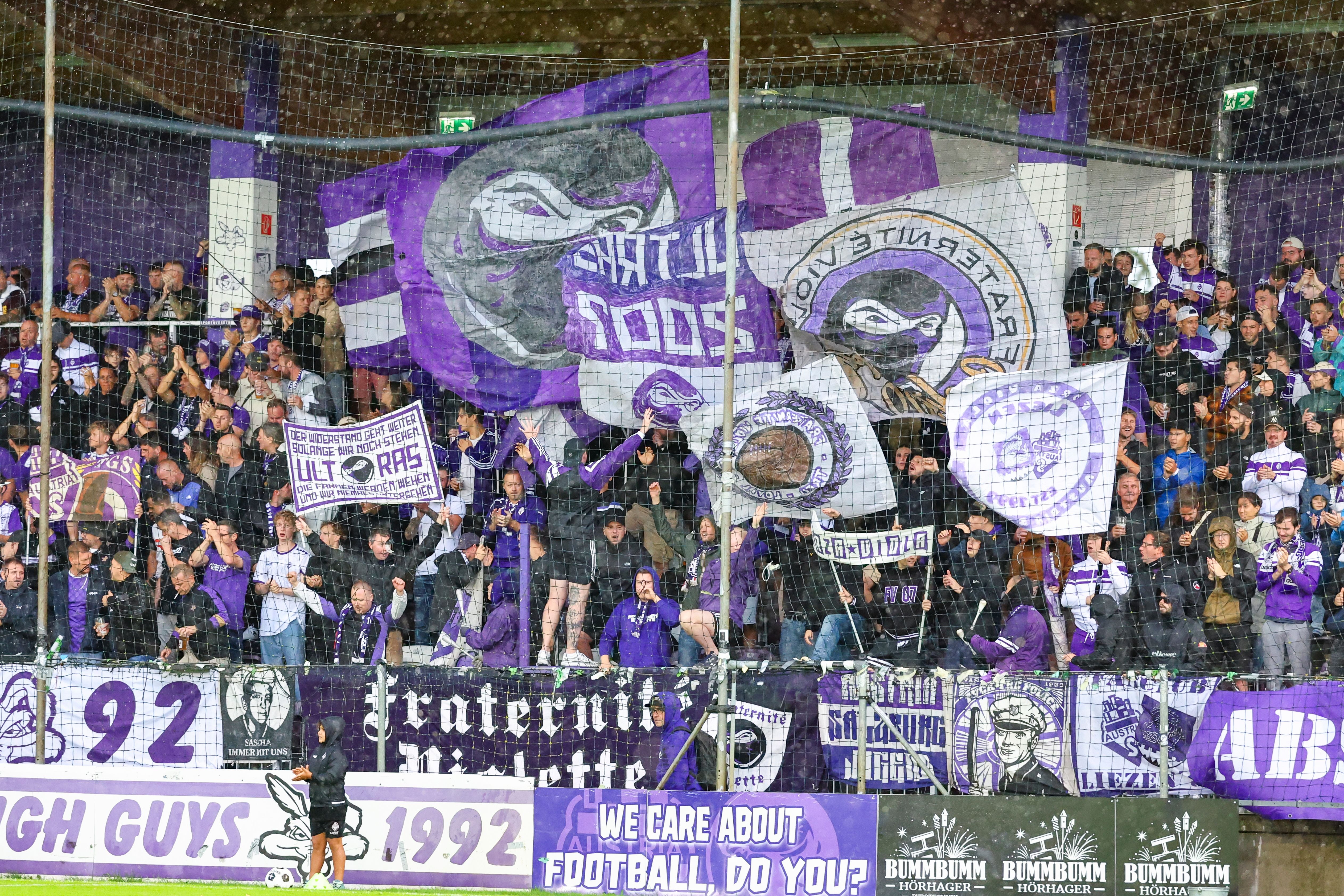 Fans von Austria Salzburg mit lila Fahnen, Transparenten und Bannern im Stadion.