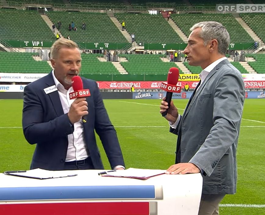 Zwei Moderatoren mit ORF-Mikrofonen führen ein Interview im Fußballstadion.