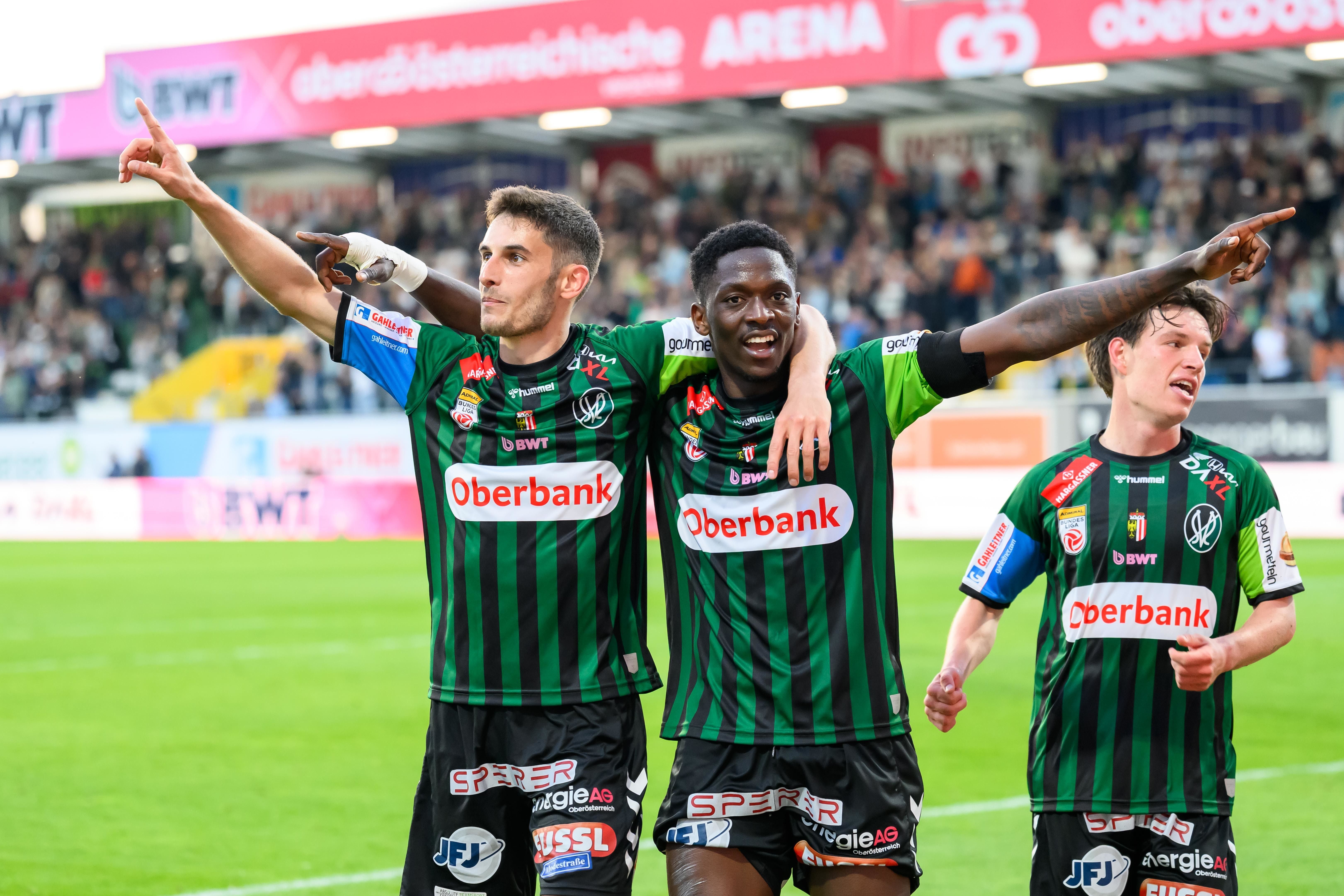 Drei Spieler der SV Ried im grün-schwarz gestreiften Trikot jubeln mit ausgebreiteten Armen auf dem Spielfeld.