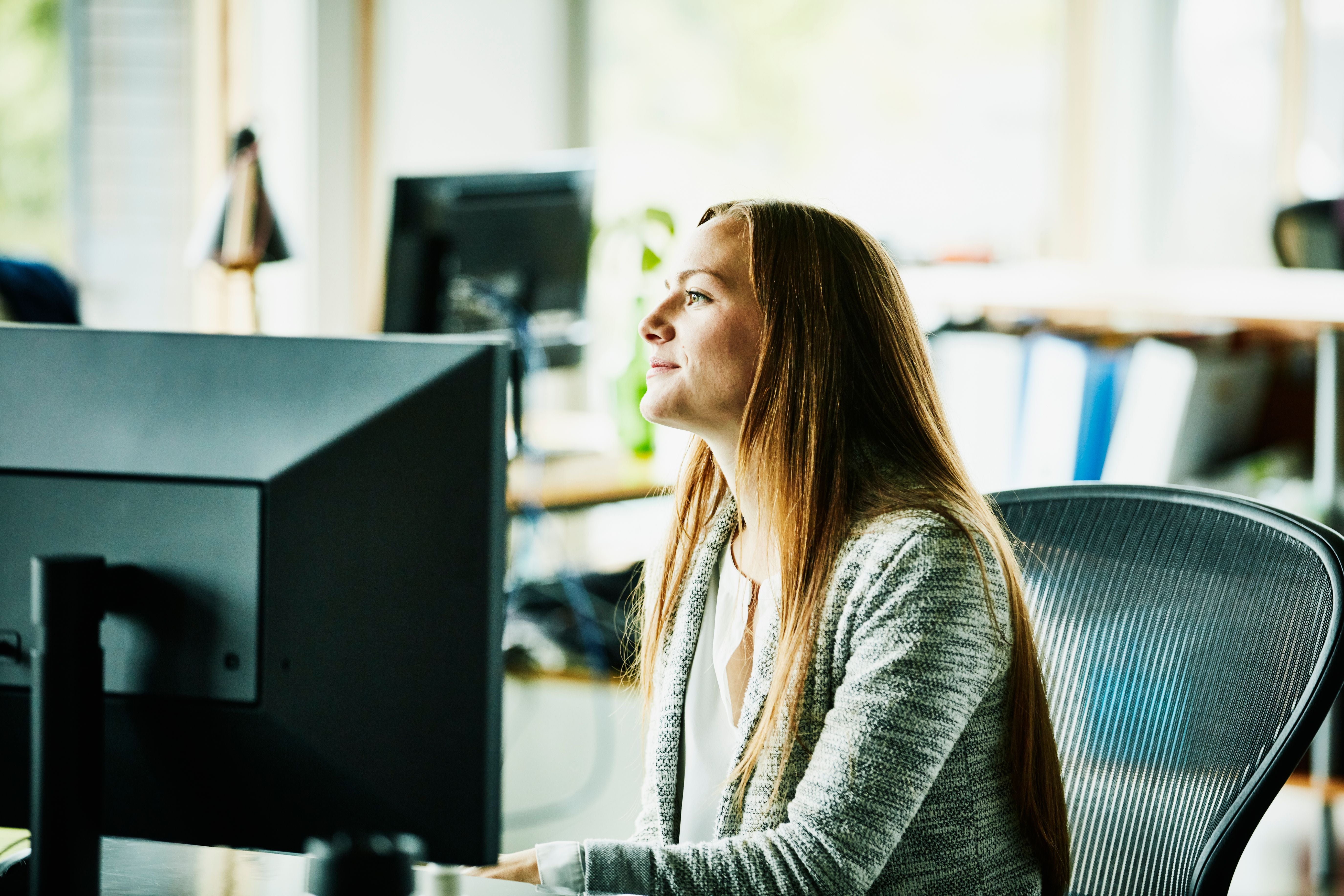 Frau sitzt an einem Schreibtisch im Büro und schaut auf einen Computerbildschirm.