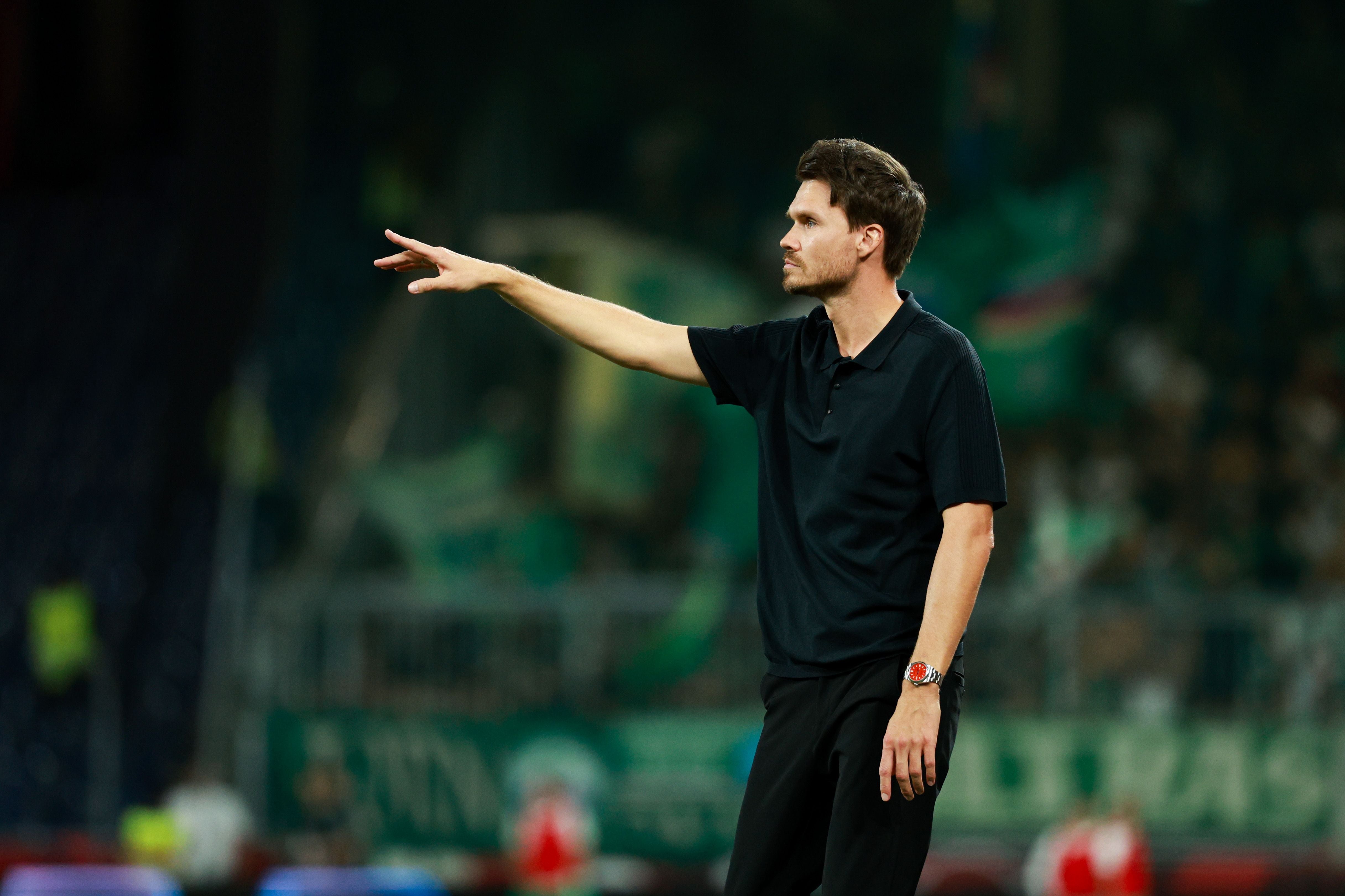 Ein Fußballtrainer im schwarzen Poloshirt gibt an der Seitenlinie Anweisungen.