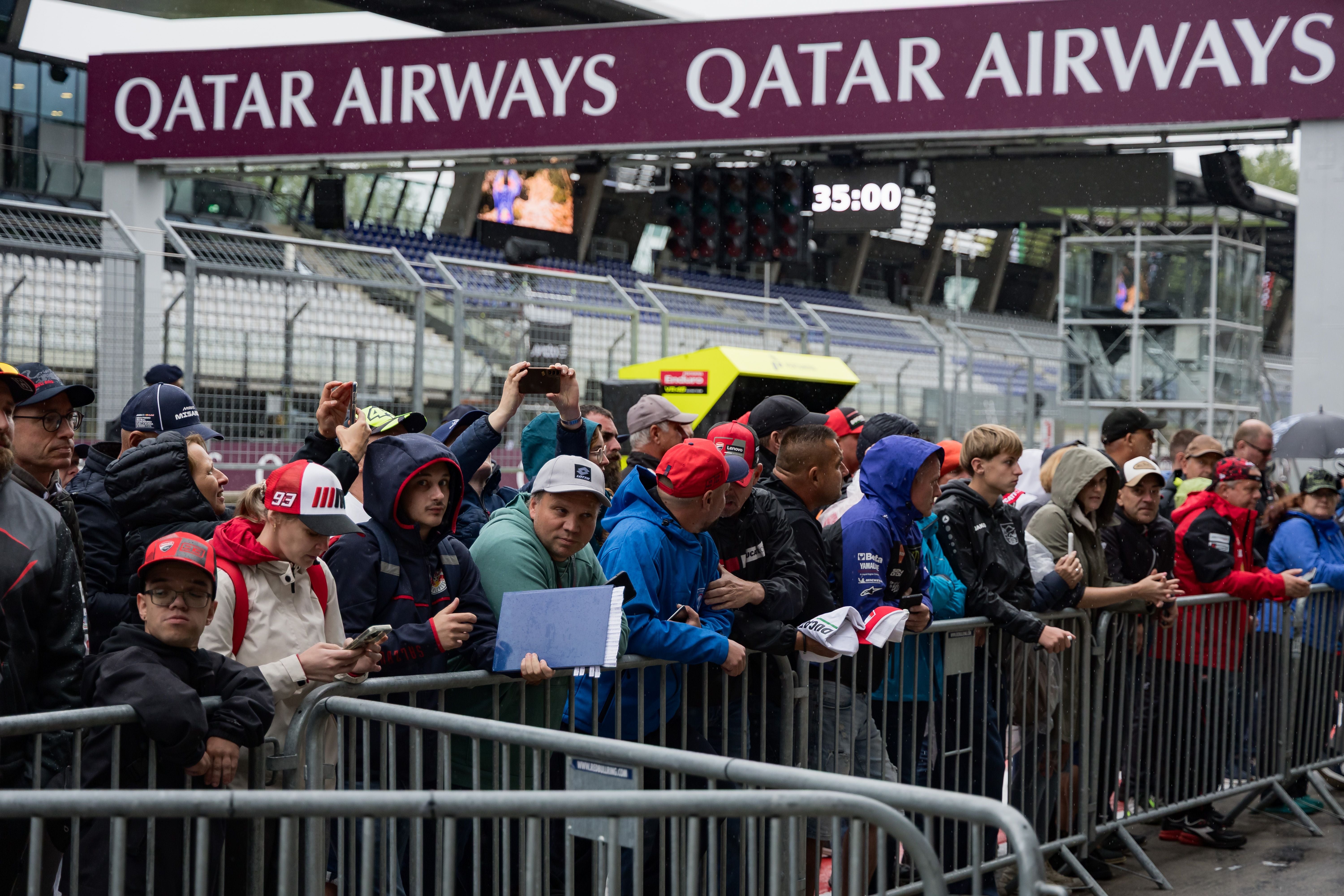 Eine Gruppe Motorsportfans steht bei Regen am Gitter im Fahrerlager des Red Bull Rings.