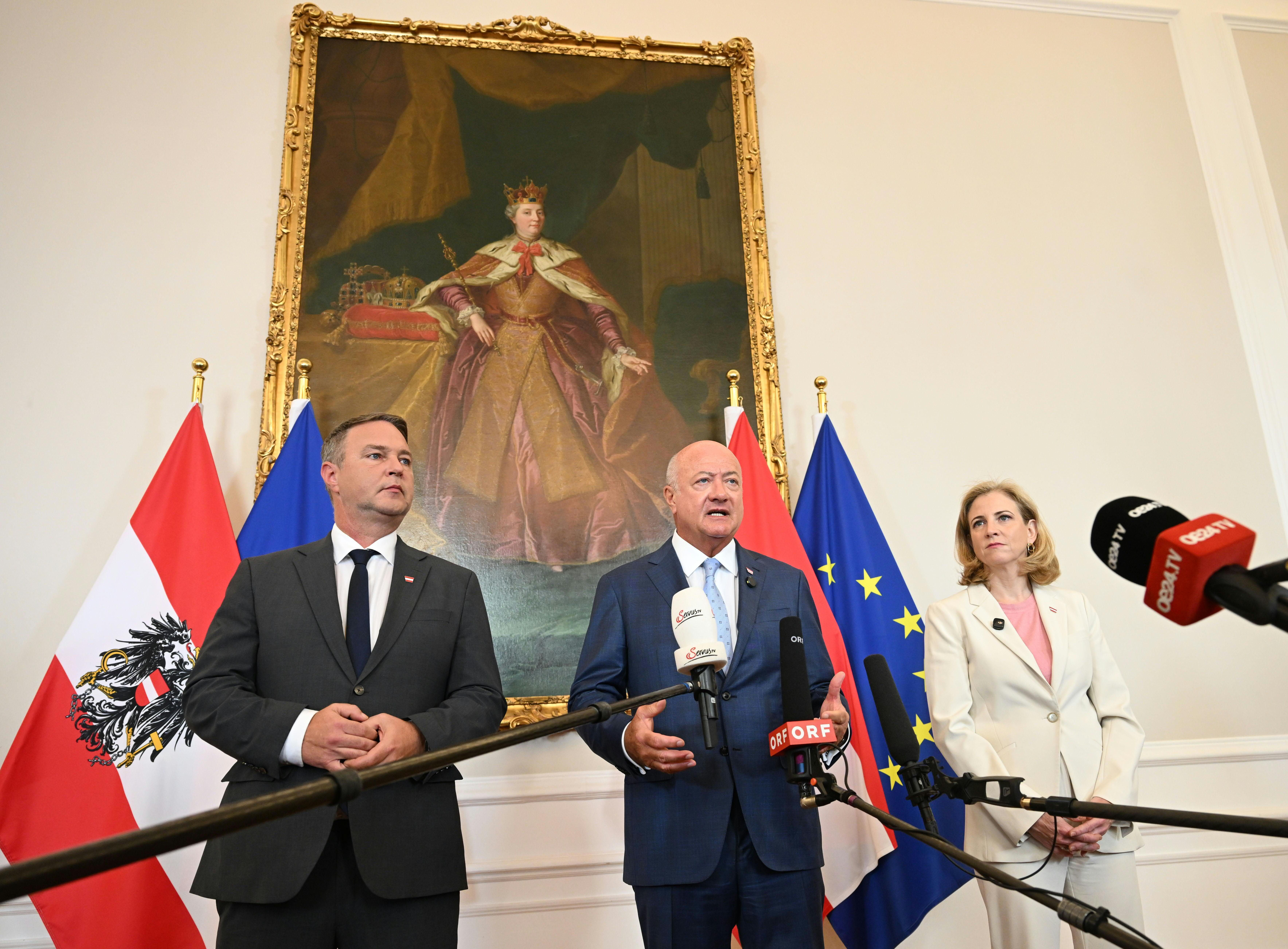 Drei Politiker bei einer Pressekonferenz vor österreichischen und EU-Flaggen im Kanzleramt Wien.
