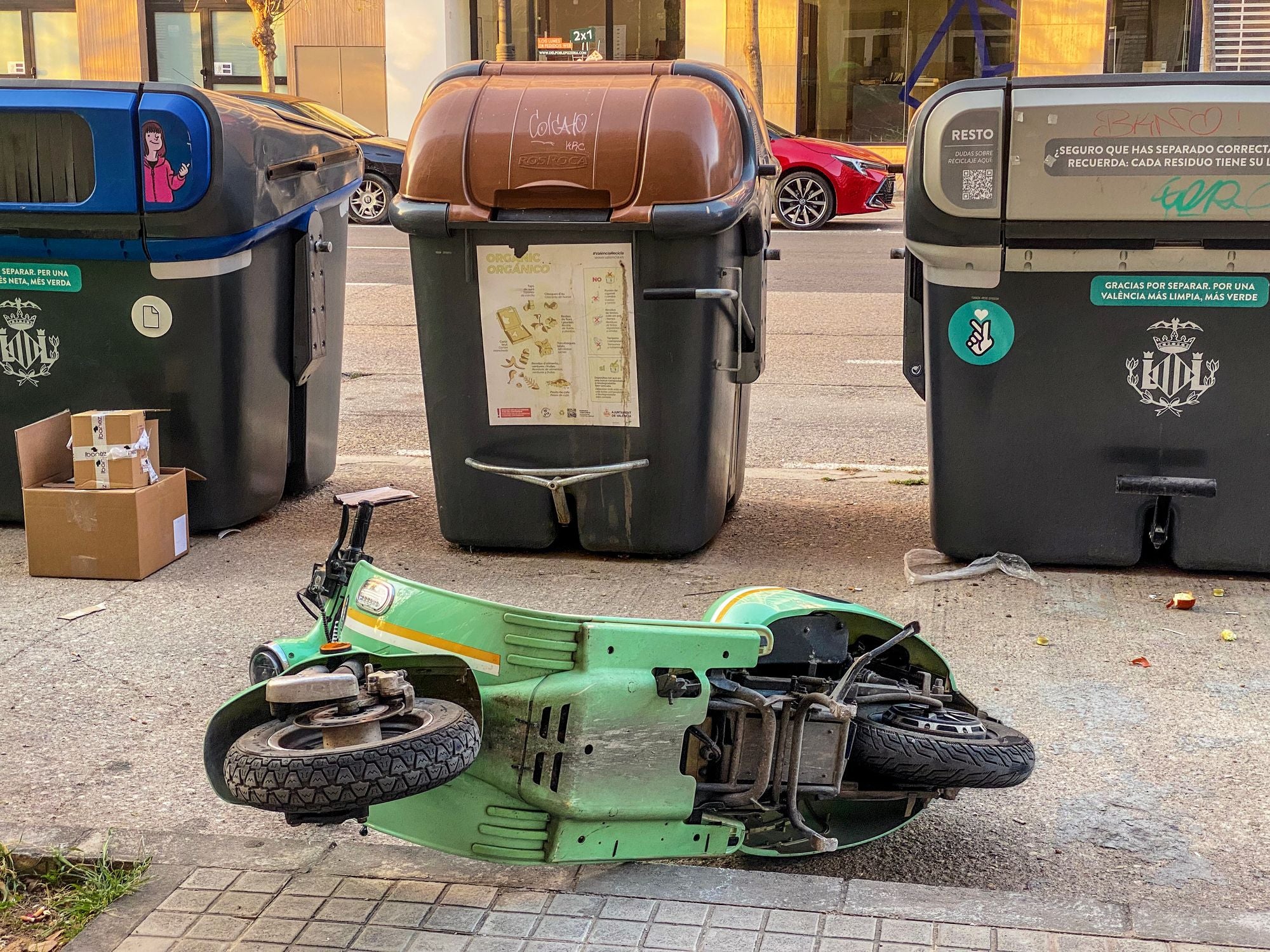 Umgekippter E-Roller liegt vor Müllcontainern auf dem Gehweg in Valencia, Spanien.