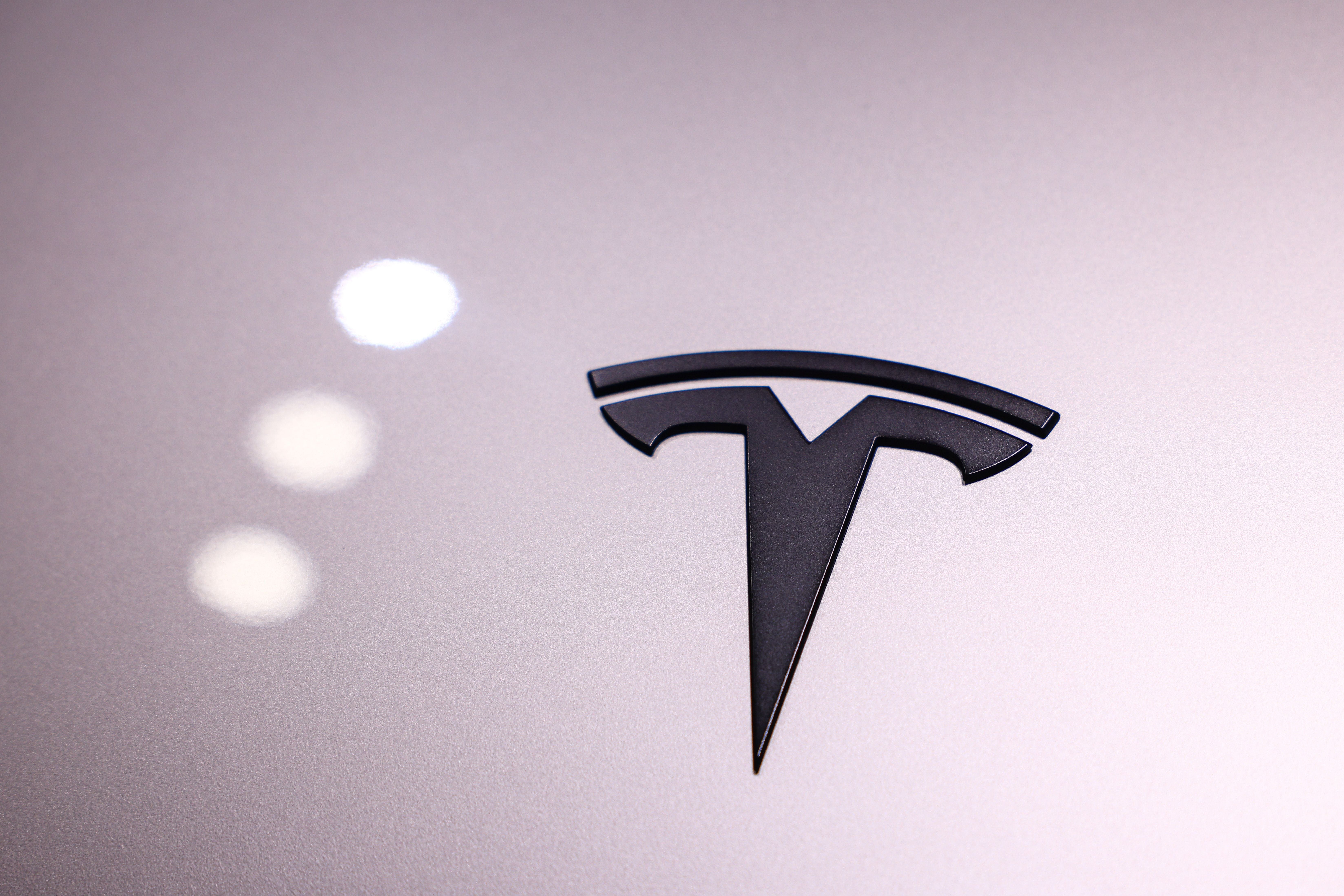 Das Tesla-Logo auf einer glatten, hellen Oberfläche mit Lichtreflexionen.