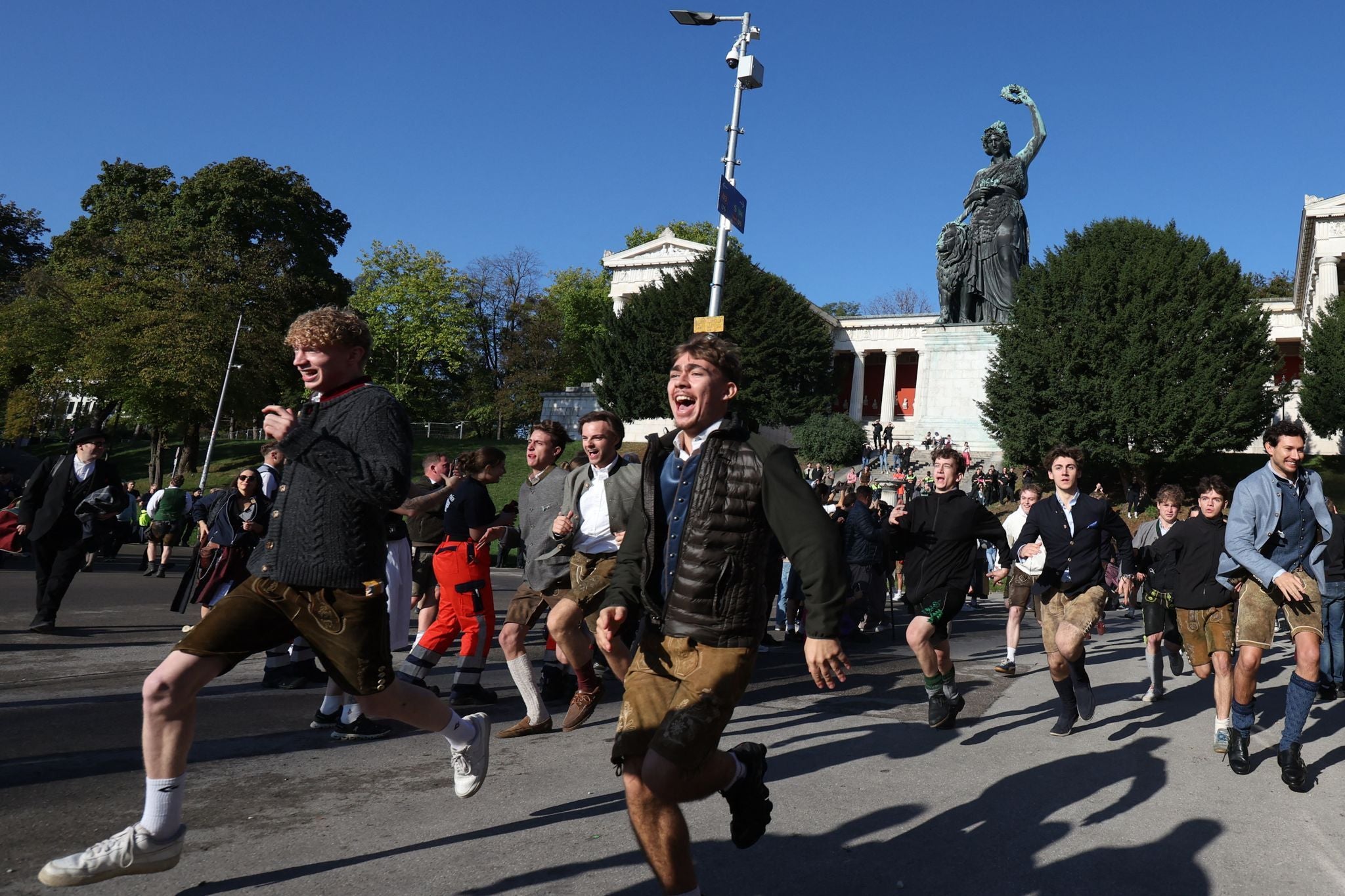 Junge Menschen in Tracht rennen lachend zum Oktoberfest auf der Münchner Theresienwiese.