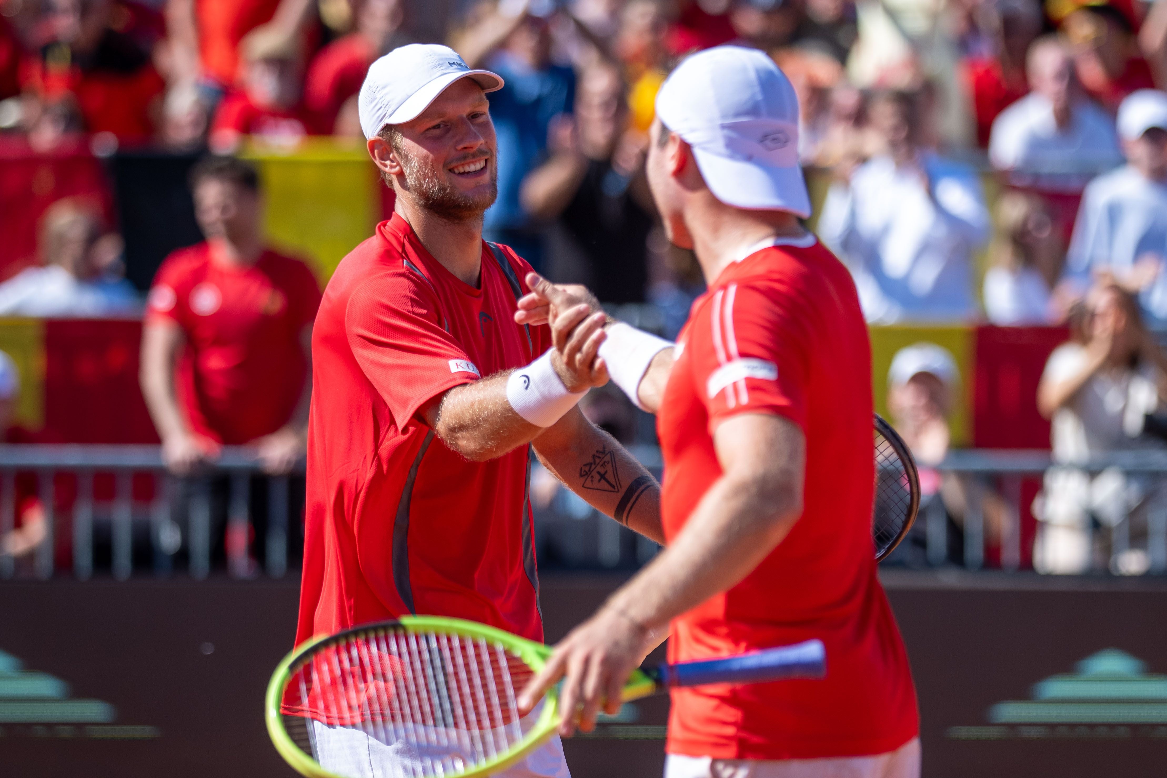 Zwei Tennisspieler im roten Trikot jubeln und gratulieren sich auf dem Platz.