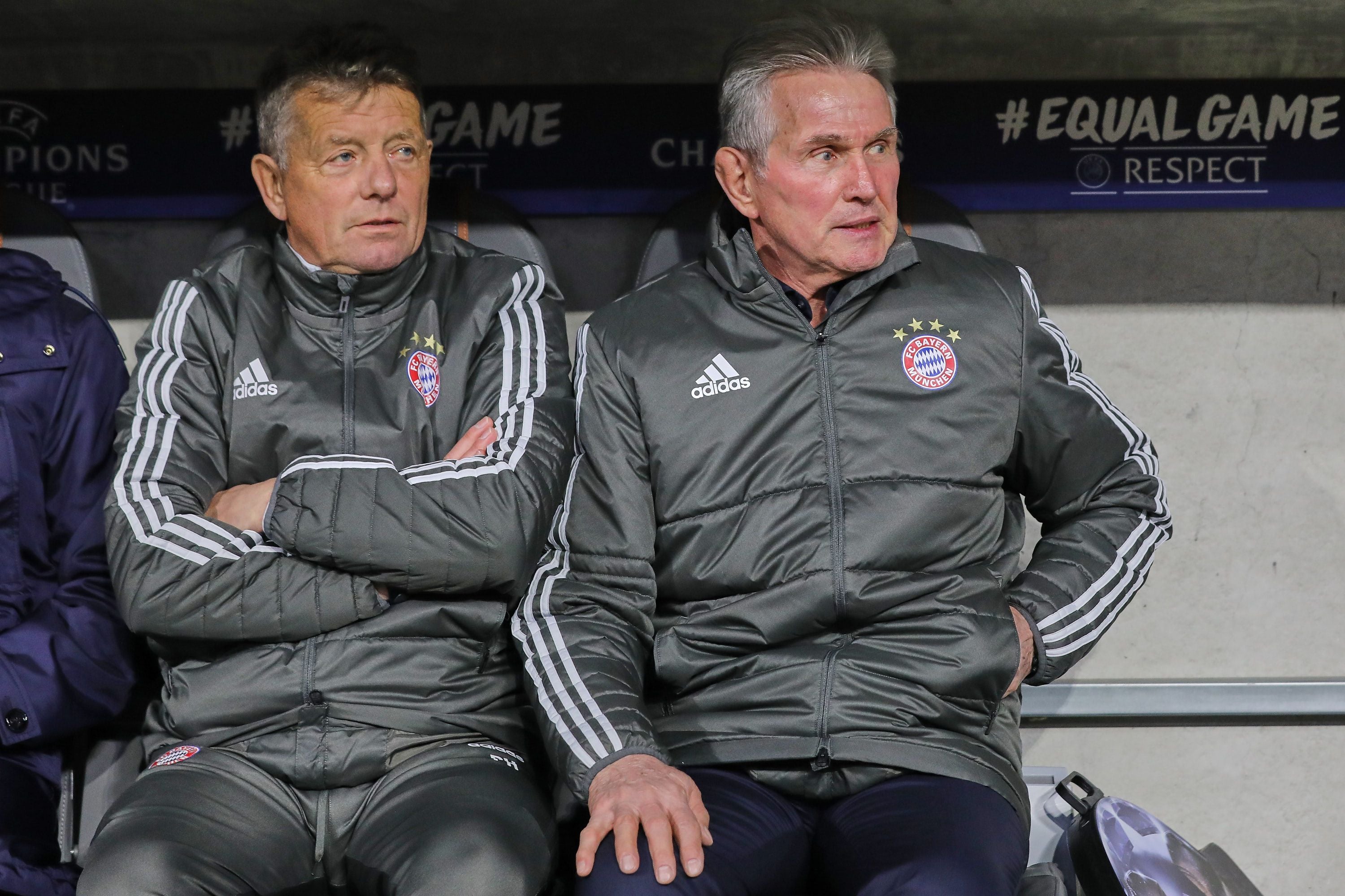 Zwei Trainer von Bayern München sitzen mit Trainingsjacken auf der Bank im Stadion.