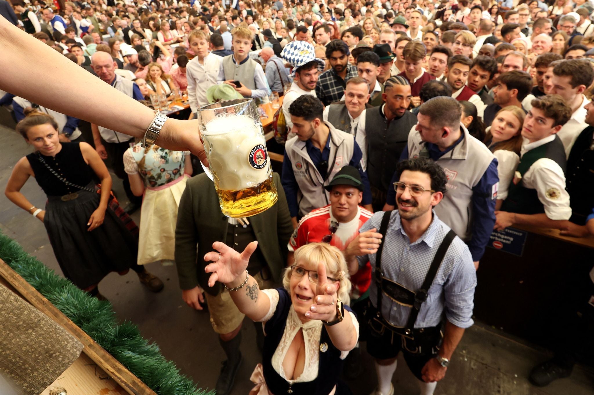 Eine Menschenmenge im Festzelt, eine Frau greift nach einem großen Bierkrug beim Oktoberfest.
