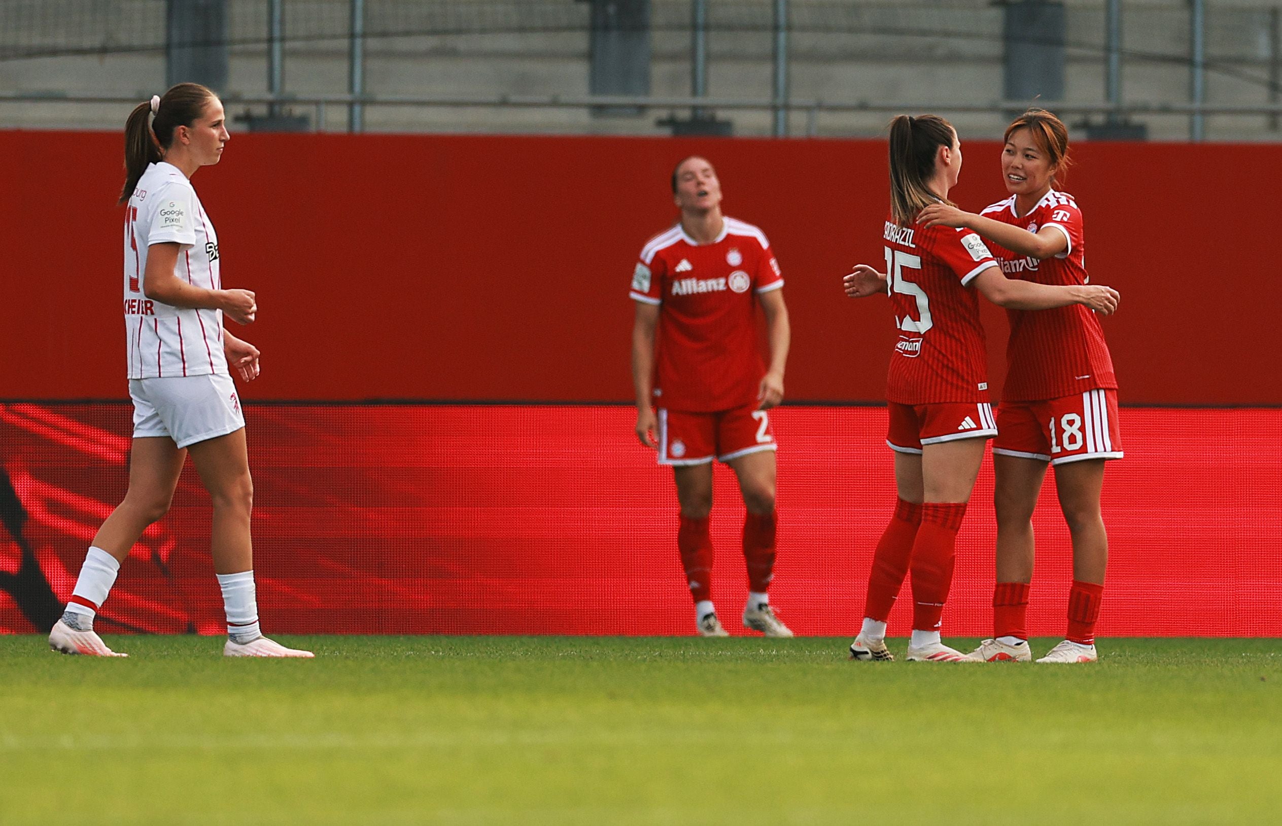 Zwei Bayern-Spielerinnen umarmen sich jubelnd, eine Freiburger Spielerin steht links daneben.