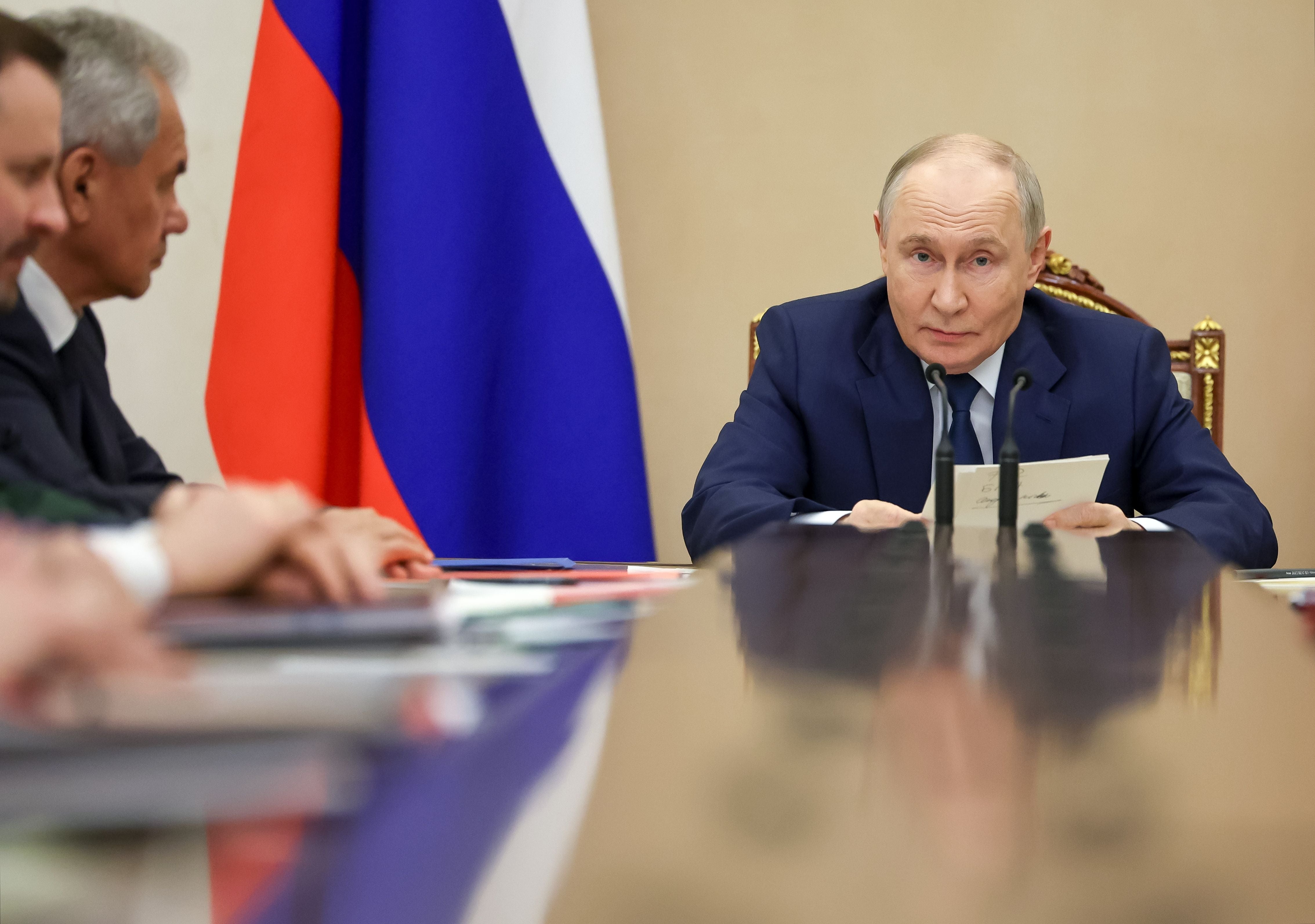 Wladimir Putin leitet eine Sitzung am Konferenztisch vor einer russischen Flagge.