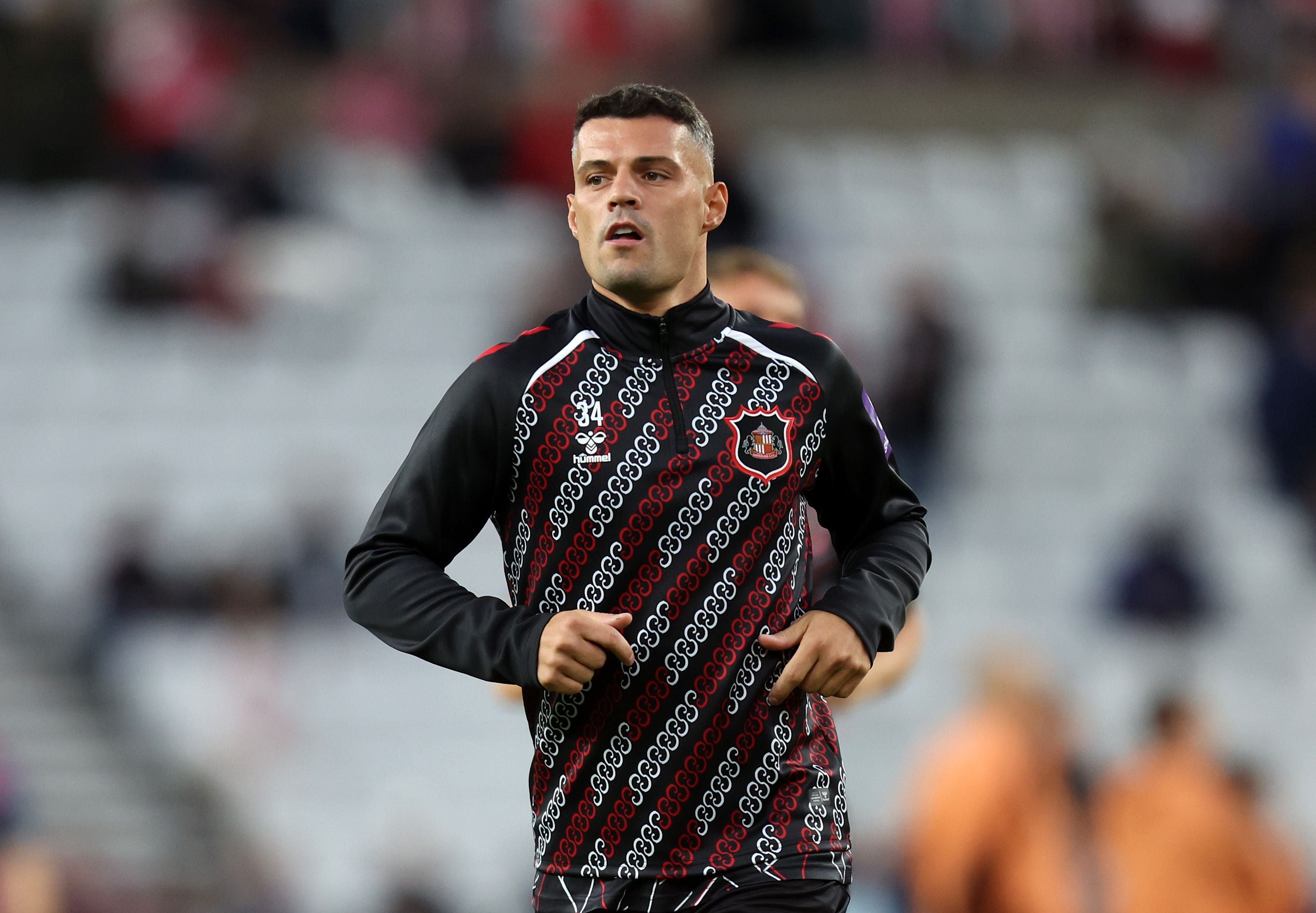 Ein Fußballspieler wärmt sich in einem schwarz-roten Trainingsanzug im Stadion auf.