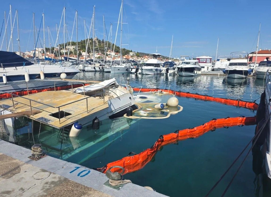 Ein teilweise gesunkenes Motorboot im Hafen, umgeben von einer orangefarbenen Absperrung.