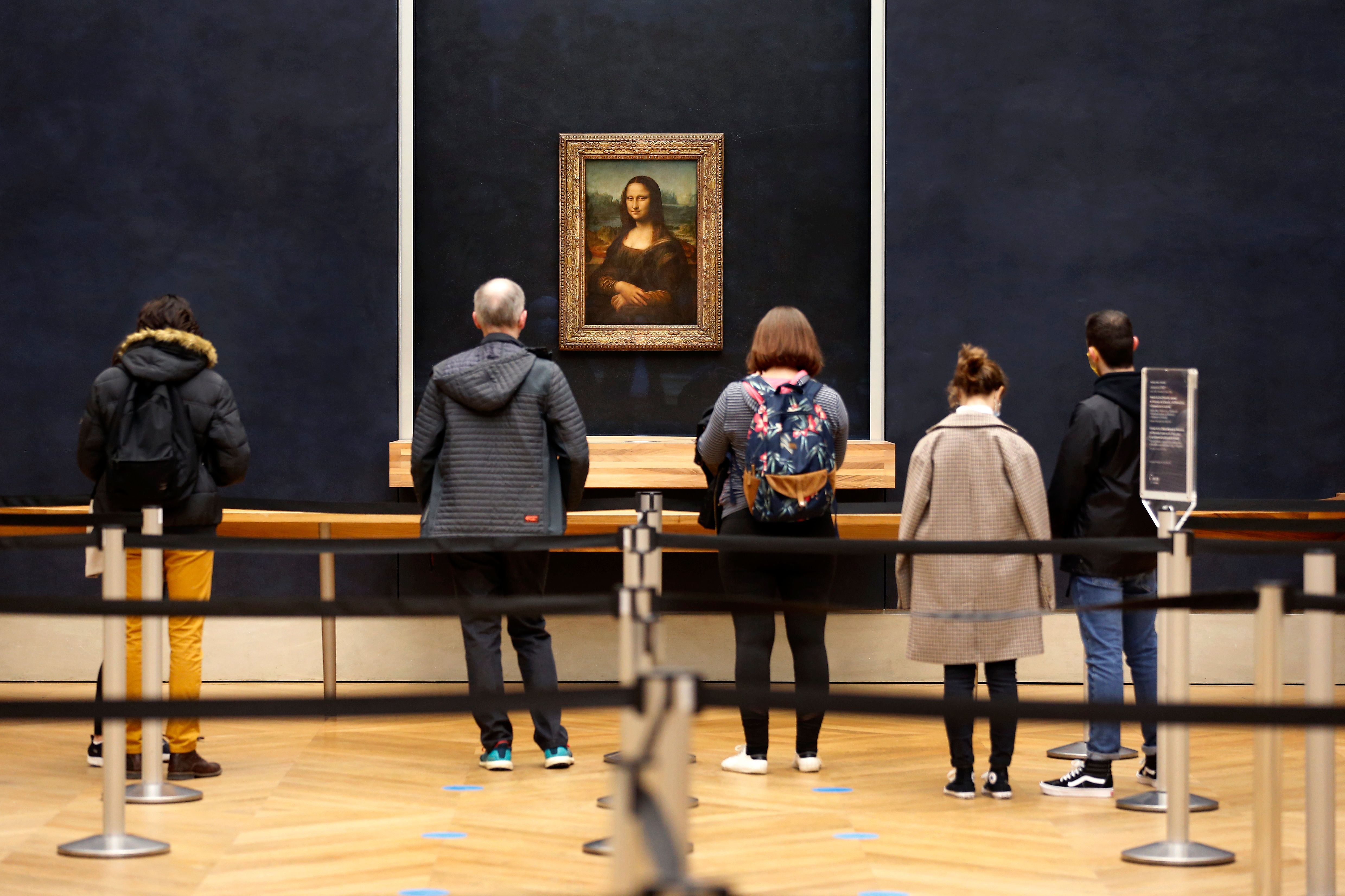 Fünf Personen betrachten die Mona Lisa im Louvre, der Raum ist fast leer.