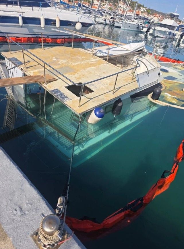 Ein teilweise gesunkenes Motorboot liegt schräg im Wasser in einem Yachthafen.