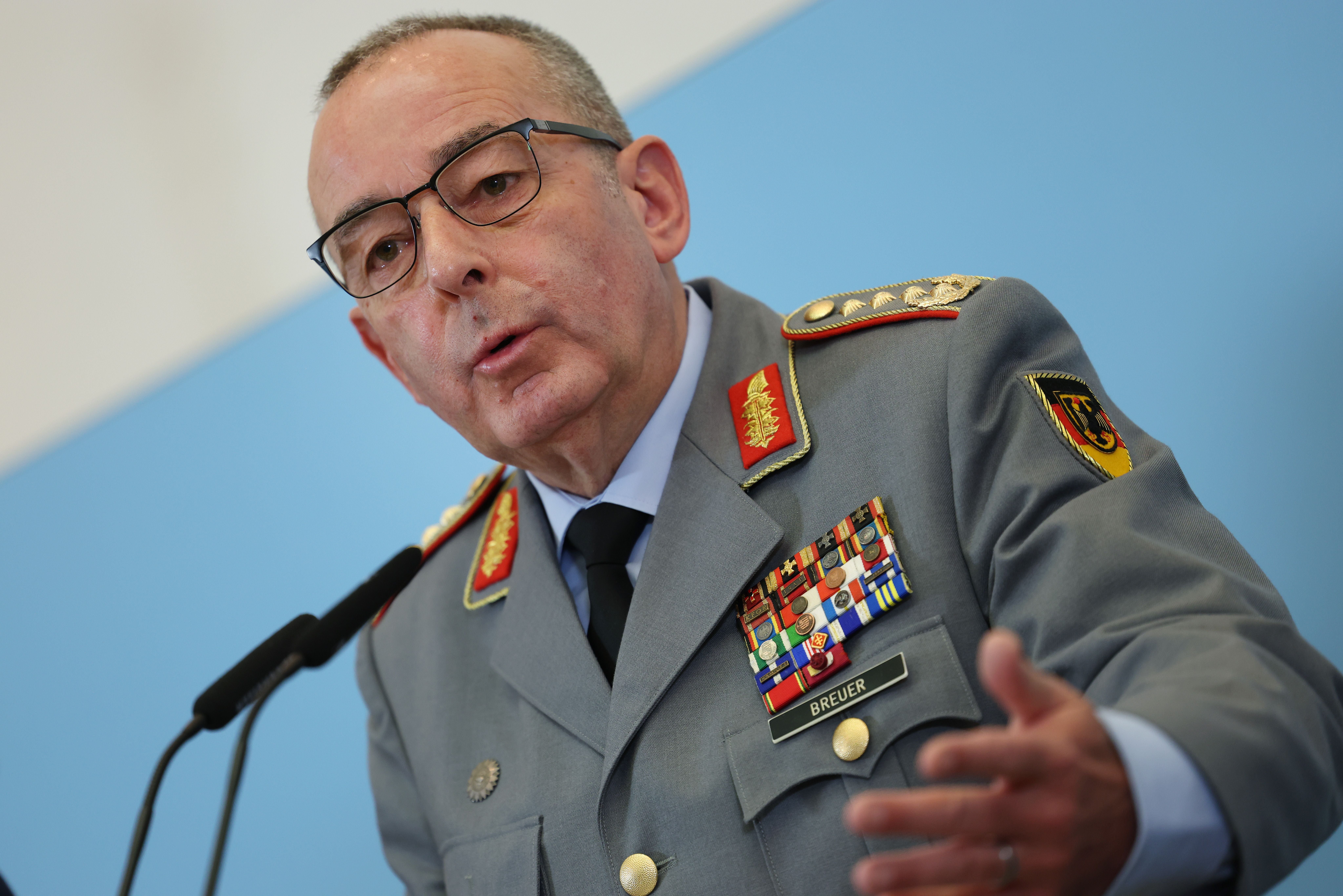 Ein deutscher General in Uniform spricht bei einer Pressekonferenz vor blauem Hintergrund.
