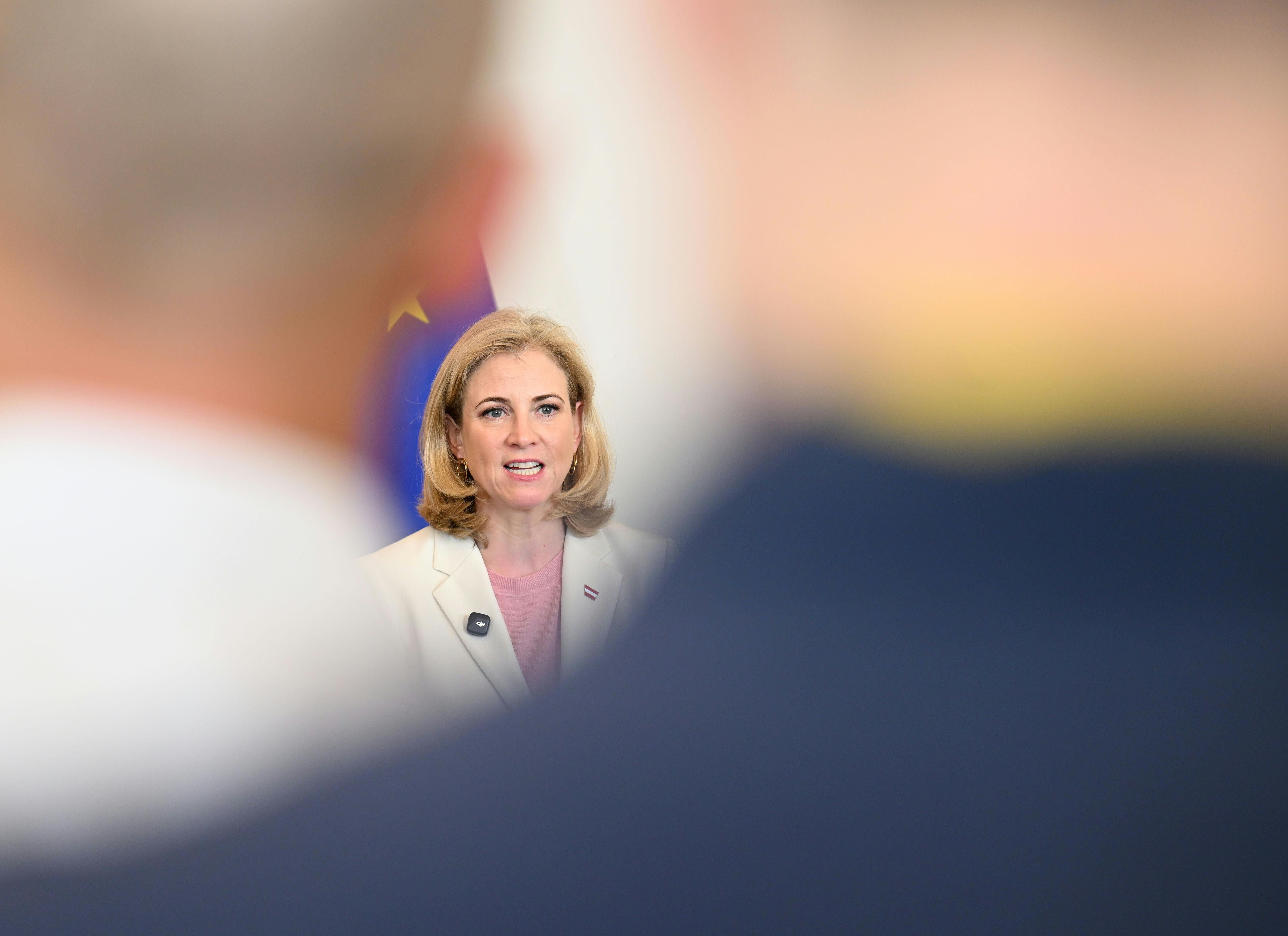 Eine Frau spricht beim Ministerrat im Bundeskanzleramt, im Vordergrund unscharfe Personen.