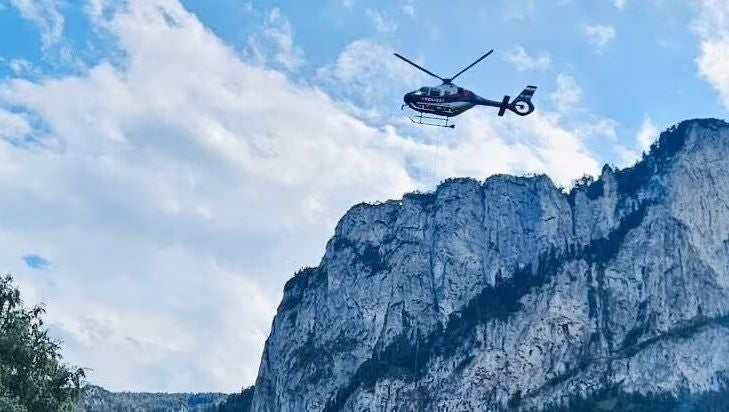 Ein Hubschrauber fliegt über felsige Berge bei Mondsee unter bewölktem Himmel.