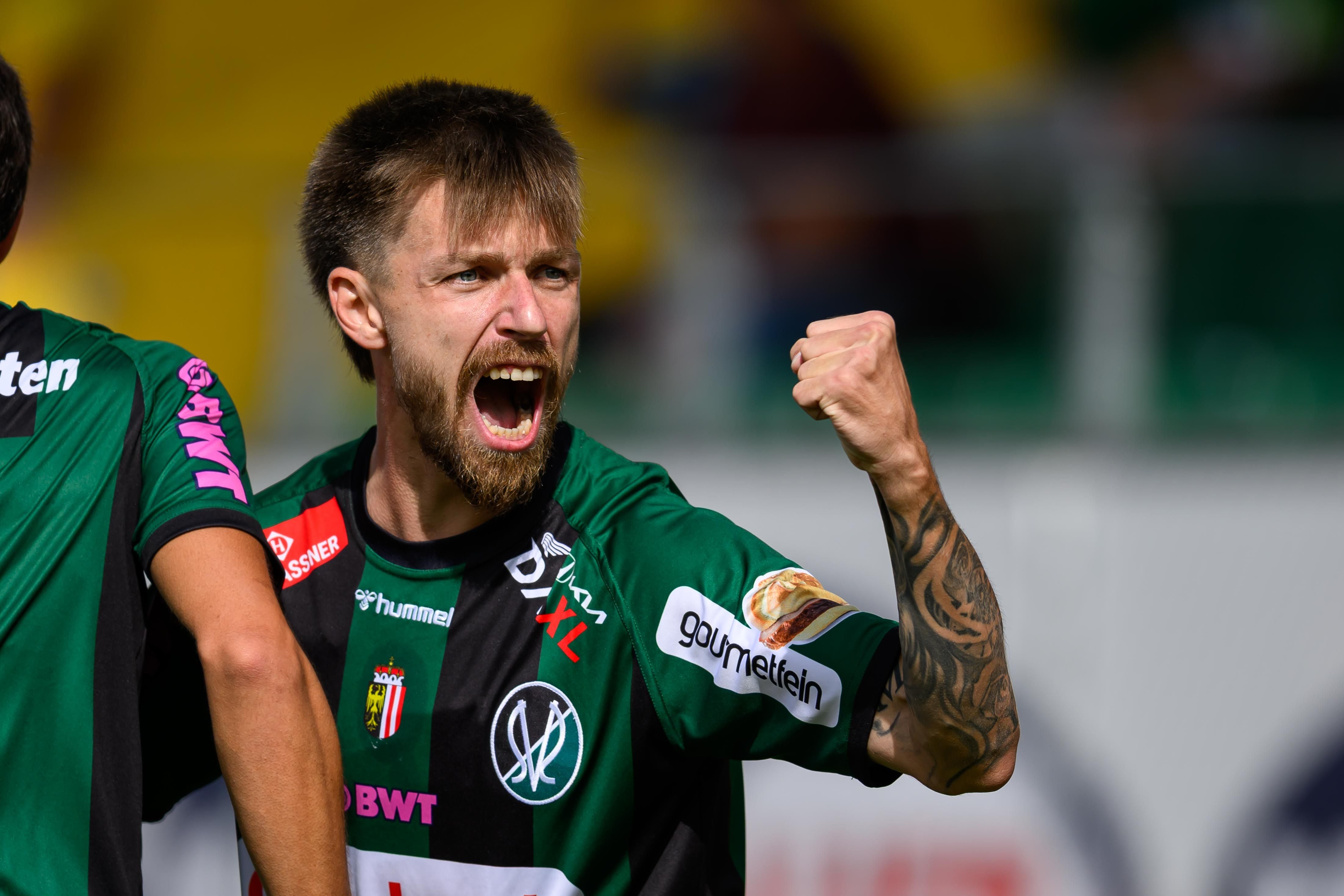 Fußballspieler im grünen Trikot jubelt mit geballter Faust und offenem Mund.