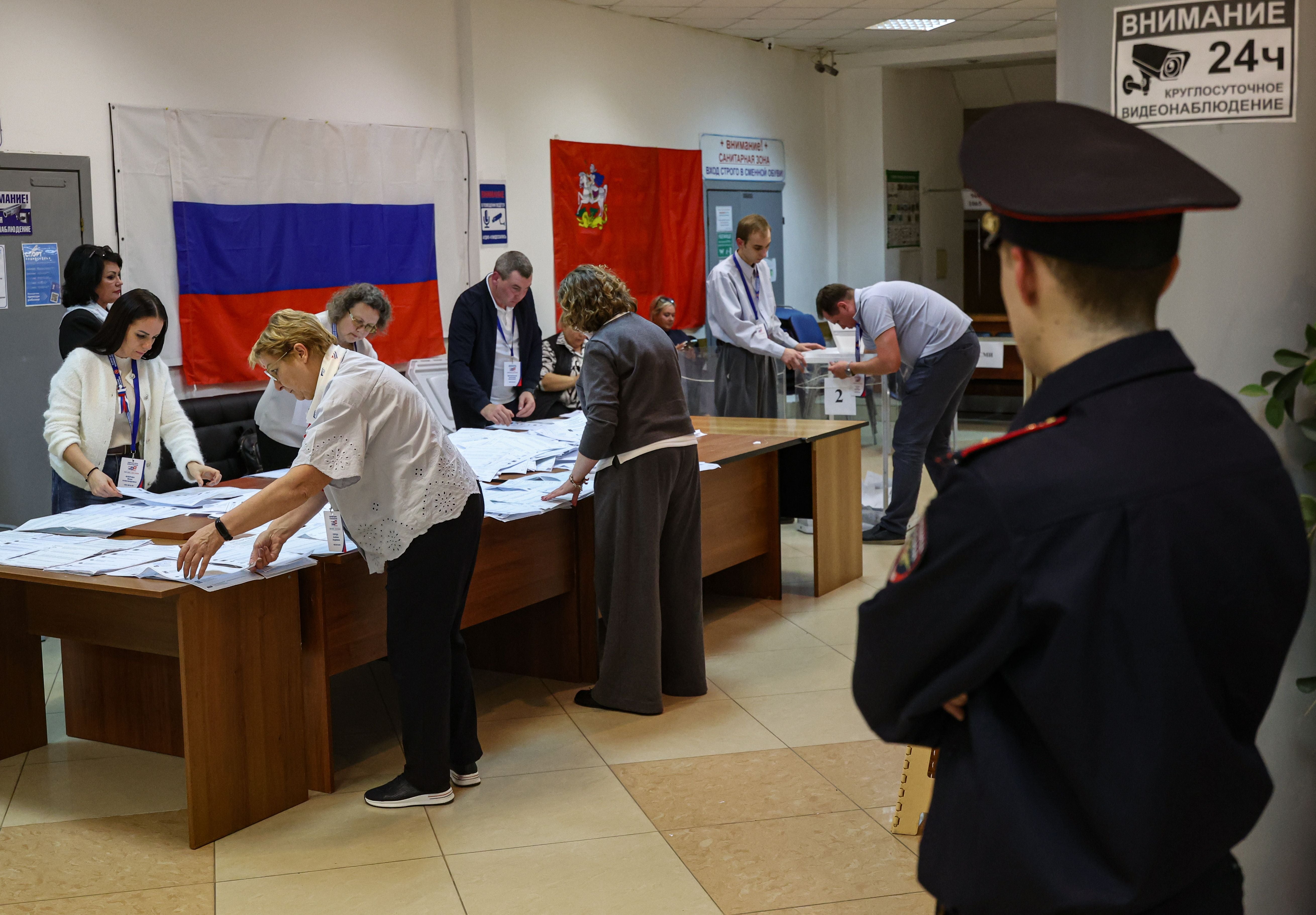 Wahlhelfer zählen Stimmzettel in einem russischen Wahllokal, ein Polizist beobachtet.