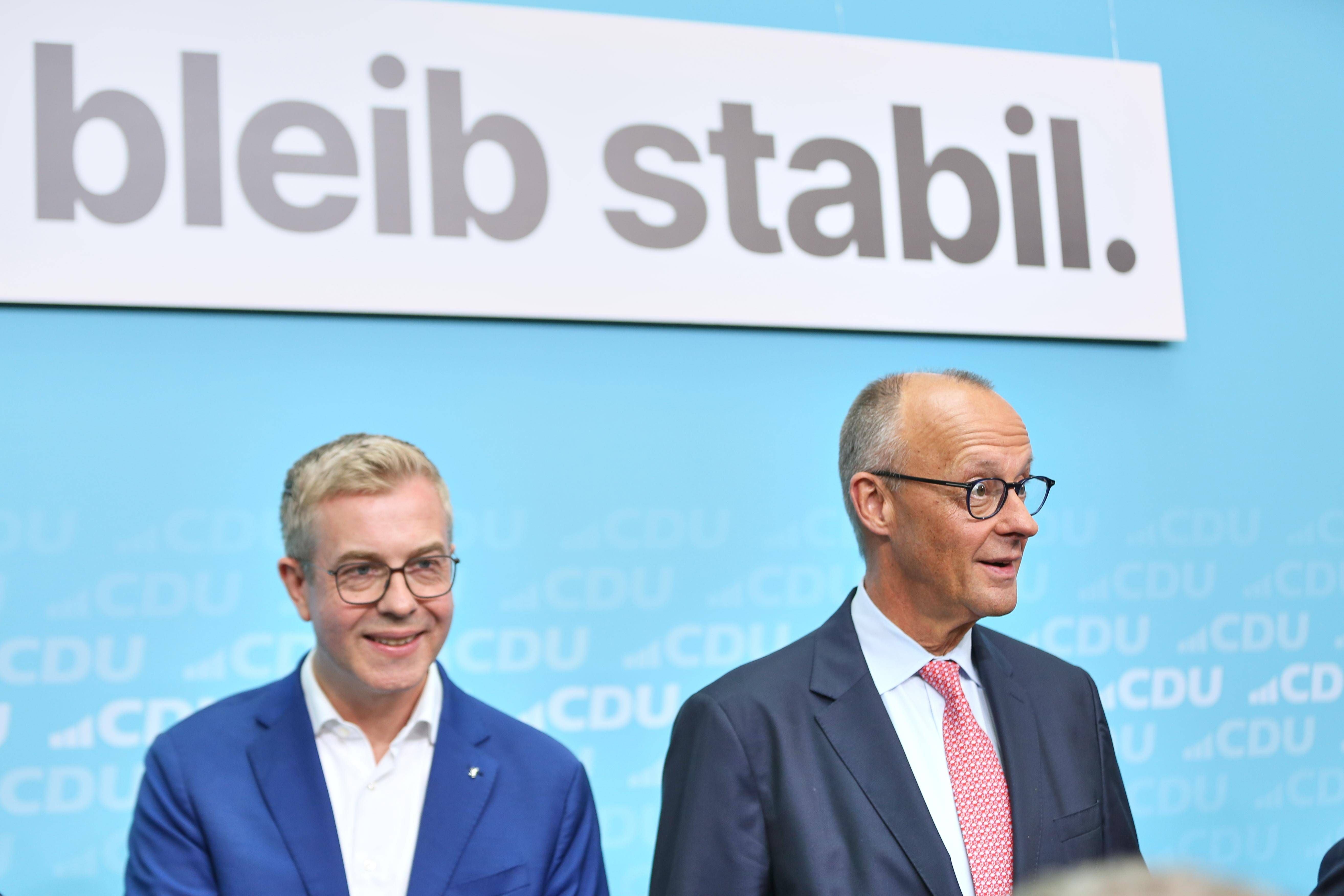 Zwei Männer im Anzug stehen vor einem Schild mit der Aufschrift "bleib stabil."