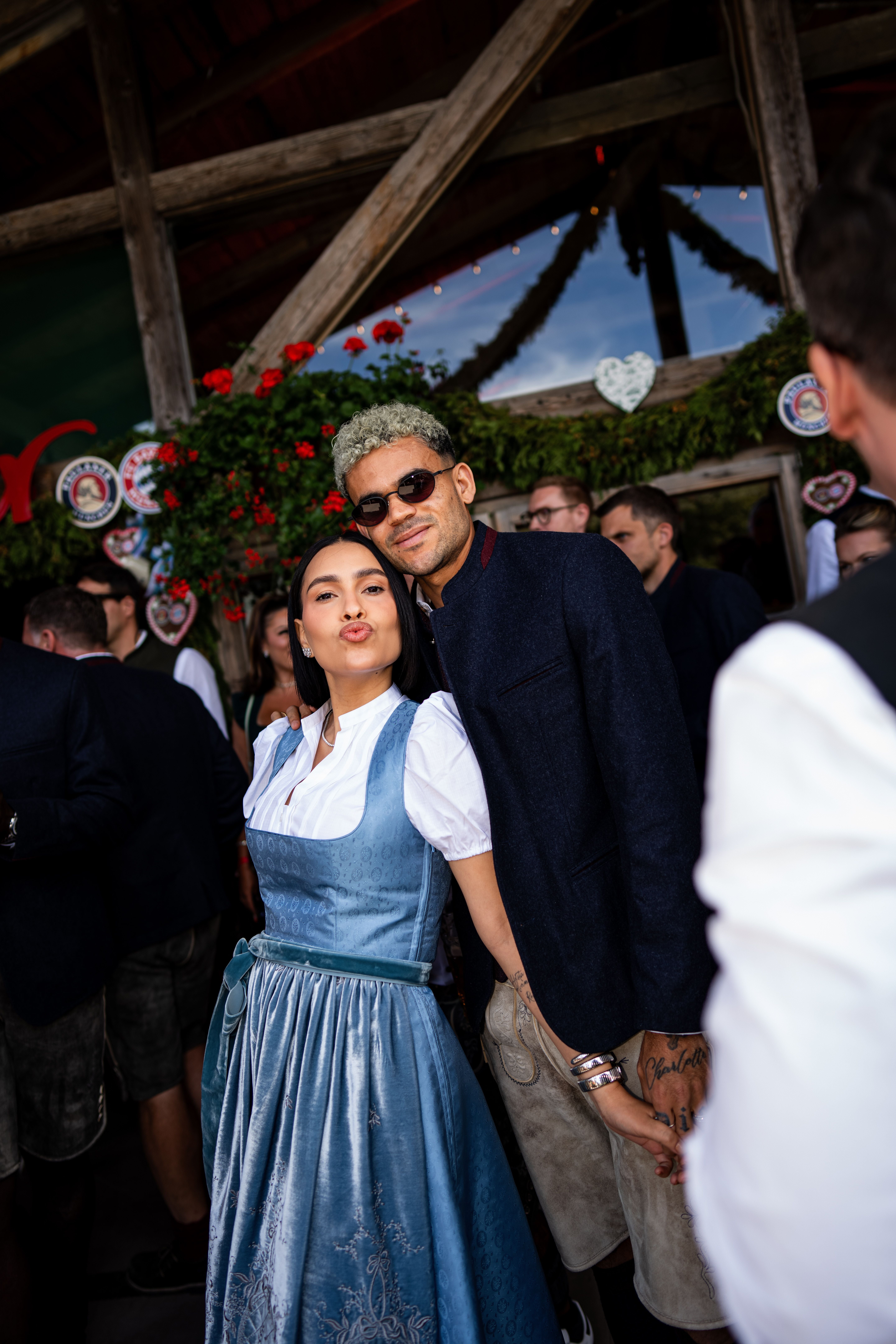 Ein Paar in traditioneller Tracht posiert lachend auf einem Oktoberfest-Event in München.