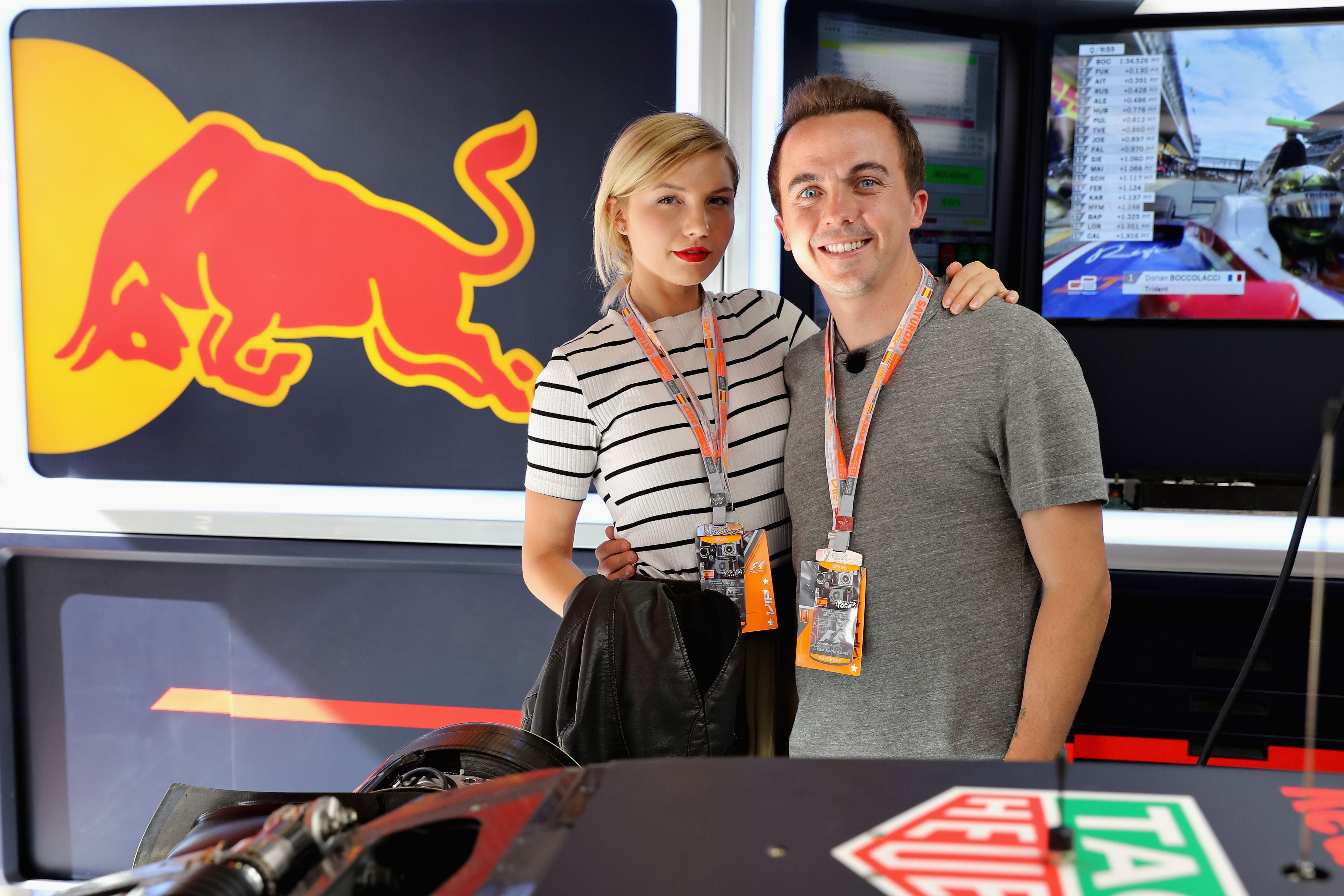 Zwei Personen posieren in der Red Bull Racing Garage vor einem Red Bull Logo und Monitoren.