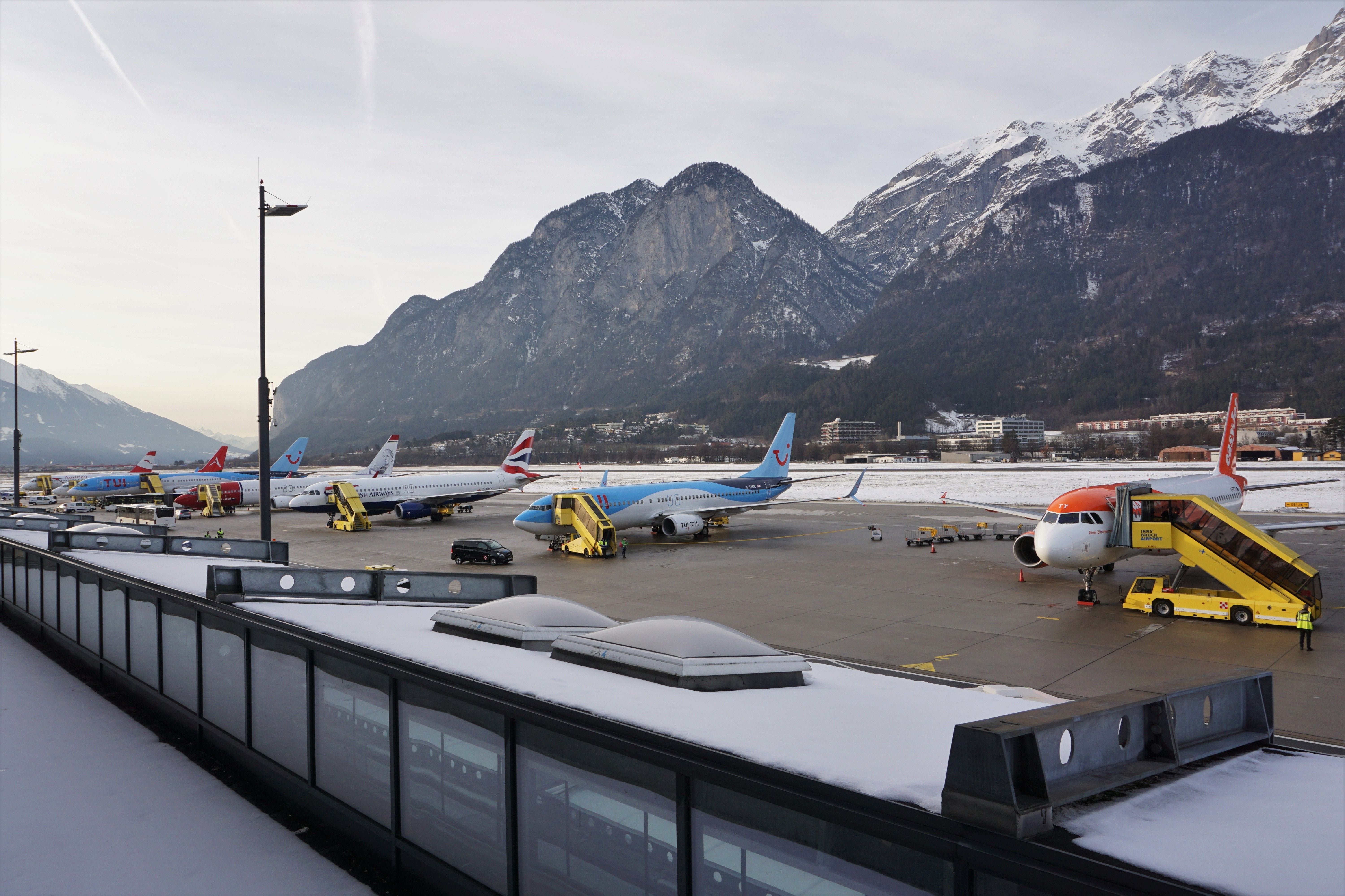 Mehrere Flugzeuge stehen am verschneiten Flughafen Innsbruck vor schneebedeckten Bergen.