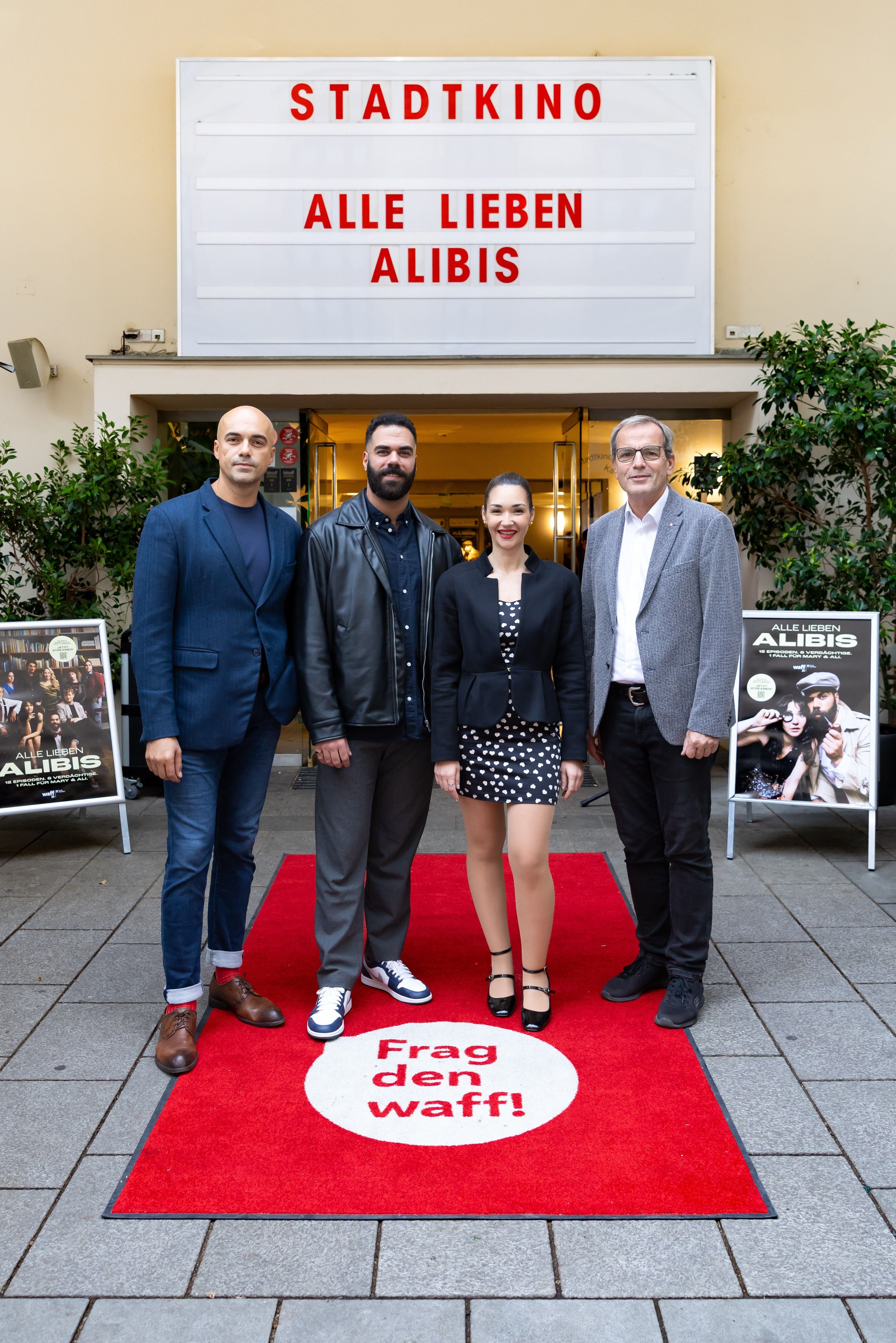 Vier Personen stehen auf einem roten Teppich vor einem Kino mit dem Schild "Alle lieben Alibis".