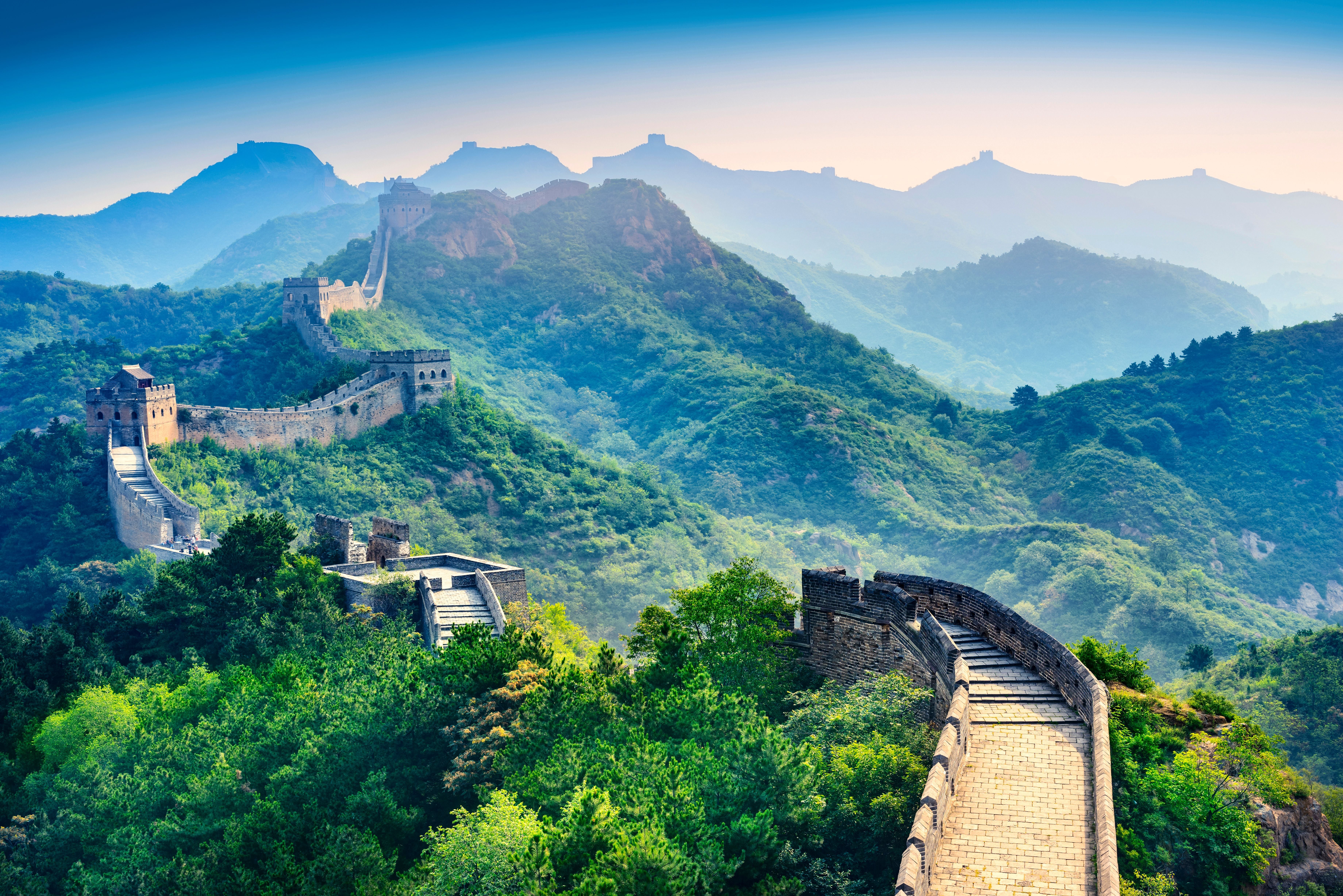 Die Chinesische Mauer schlängelt sich durch grüne Berge unter blauem Himmel.