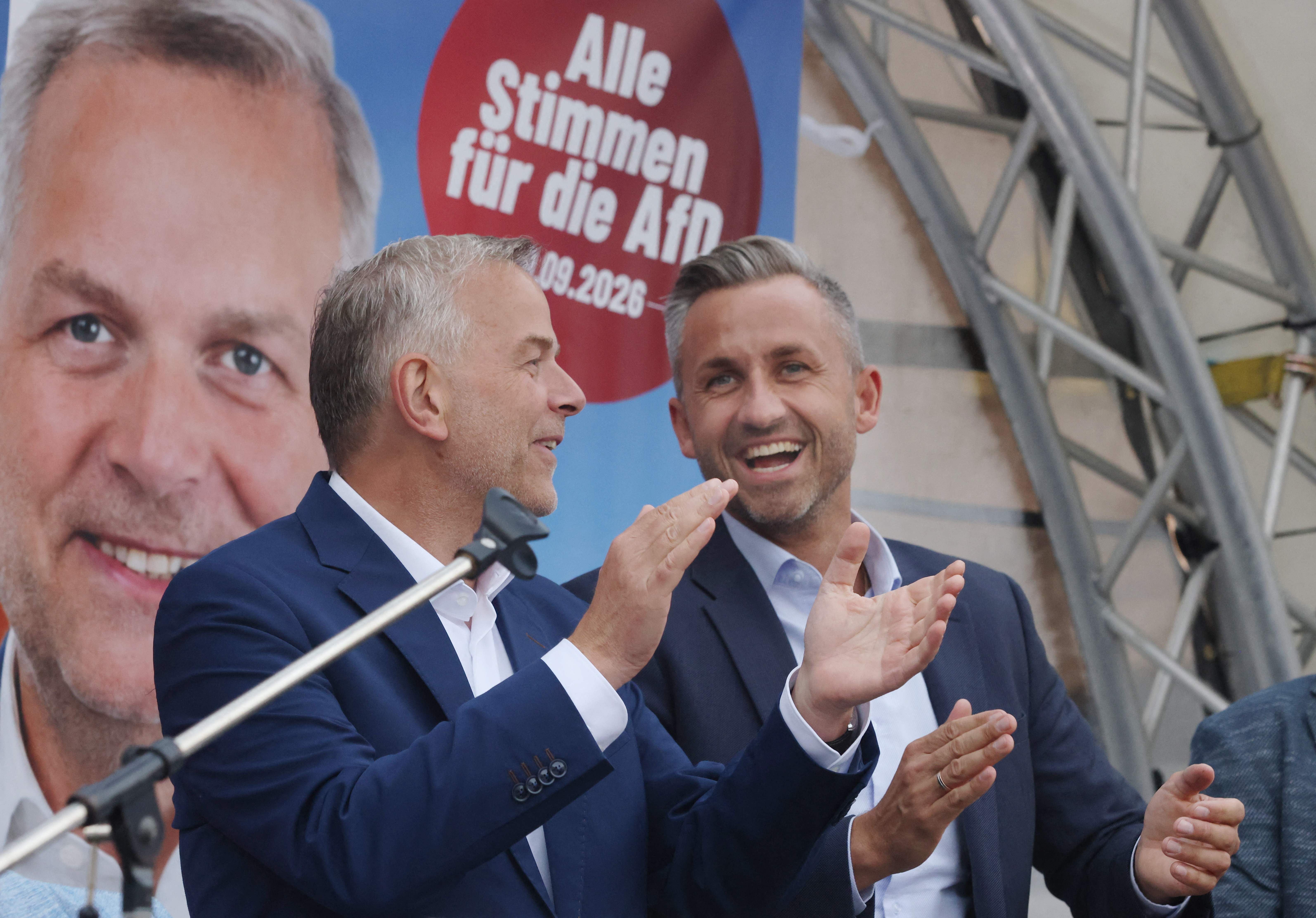 Zwei Männer im Anzug applaudieren lächelnd auf einer Wahlkampfveranstaltung der AfD.