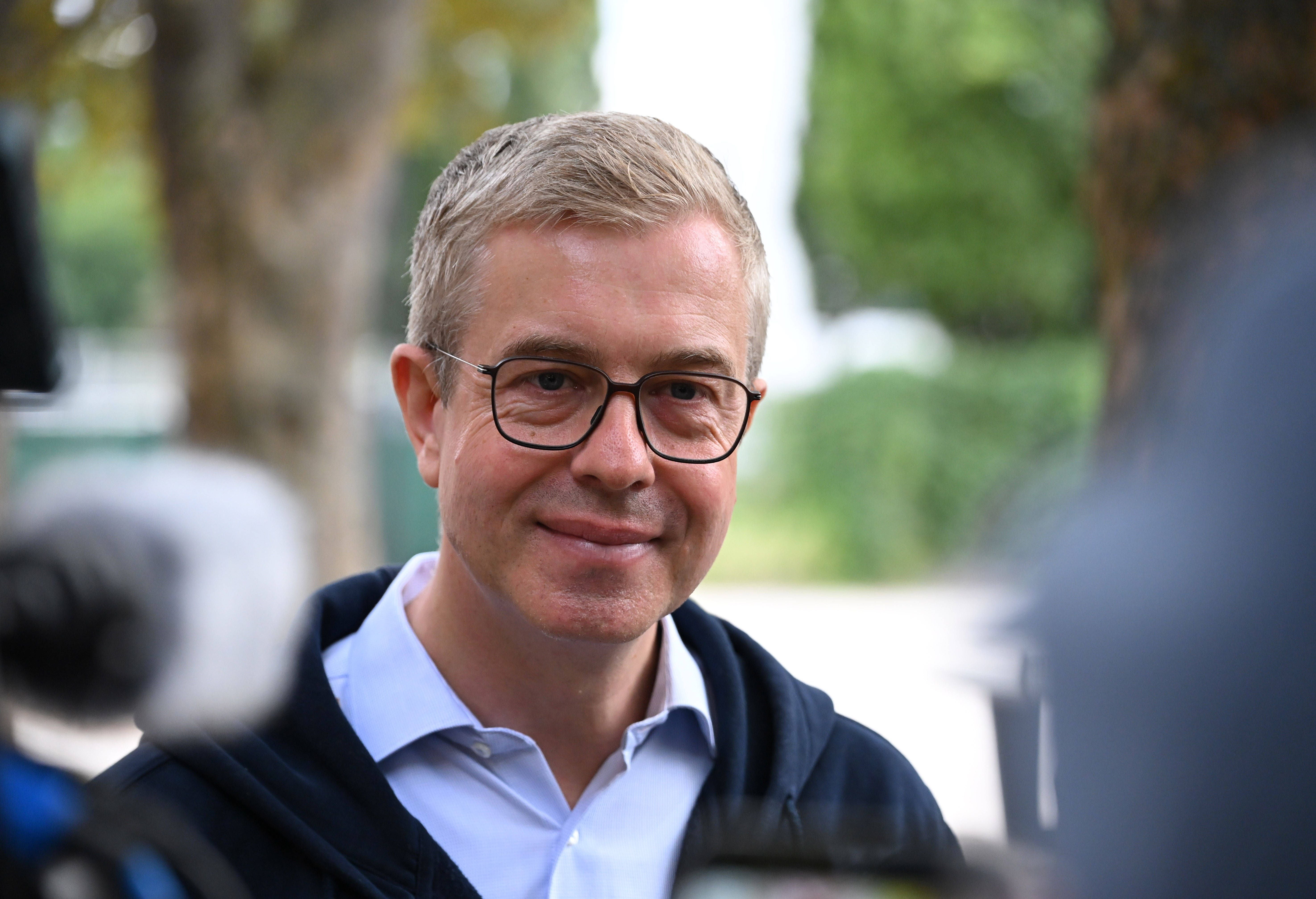 Ein Mann mit Brille lächelt im Freien und spricht mit Journalisten.