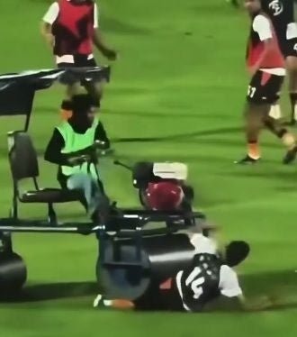 Ein Fußballspieler stürzt vor einem Krankenwagen auf dem Spielfeld, umgeben von anderen Spielern.