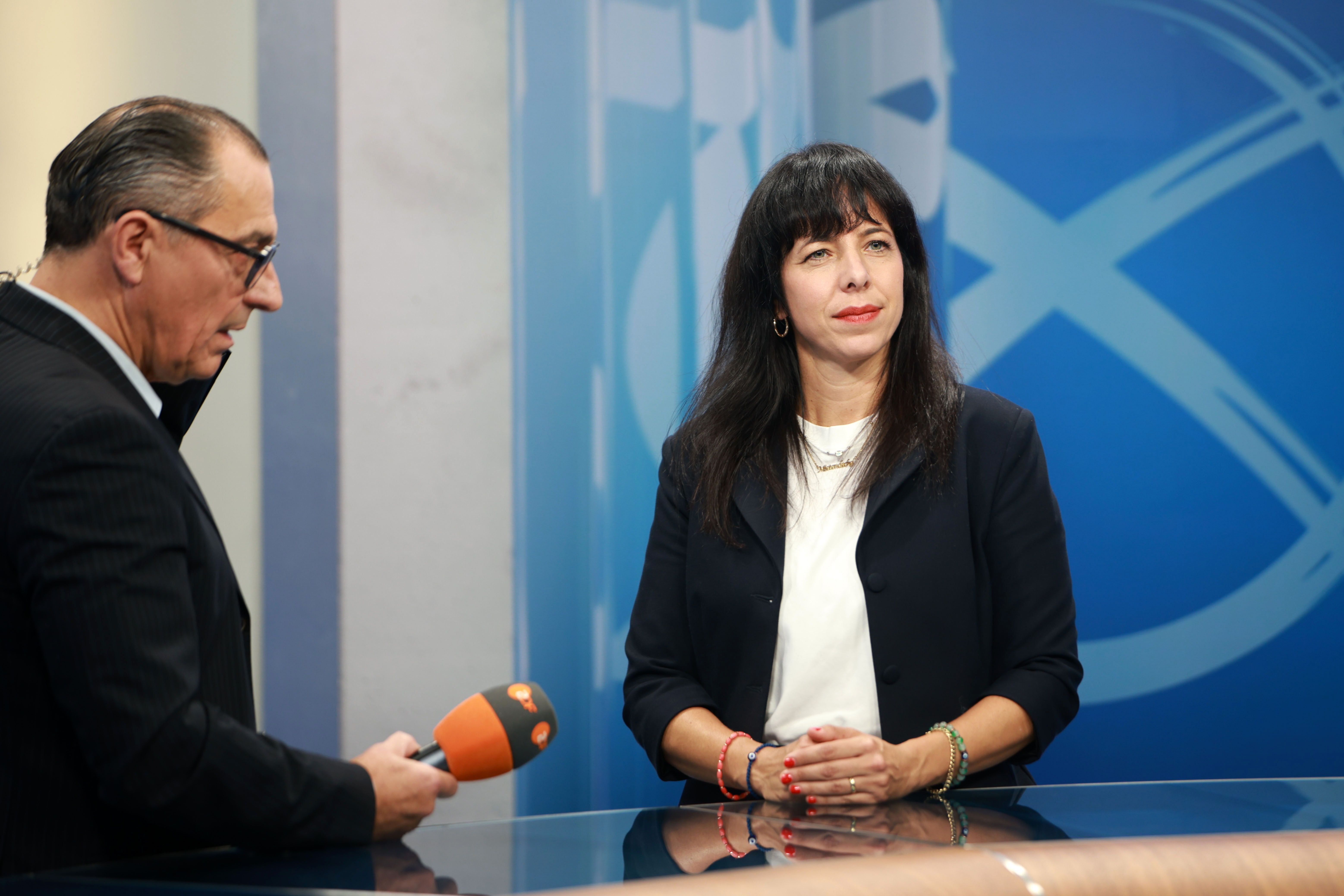 Eine Frau und ein Mann bei einem TV-Interview im Studio mit blauem Hintergrund.