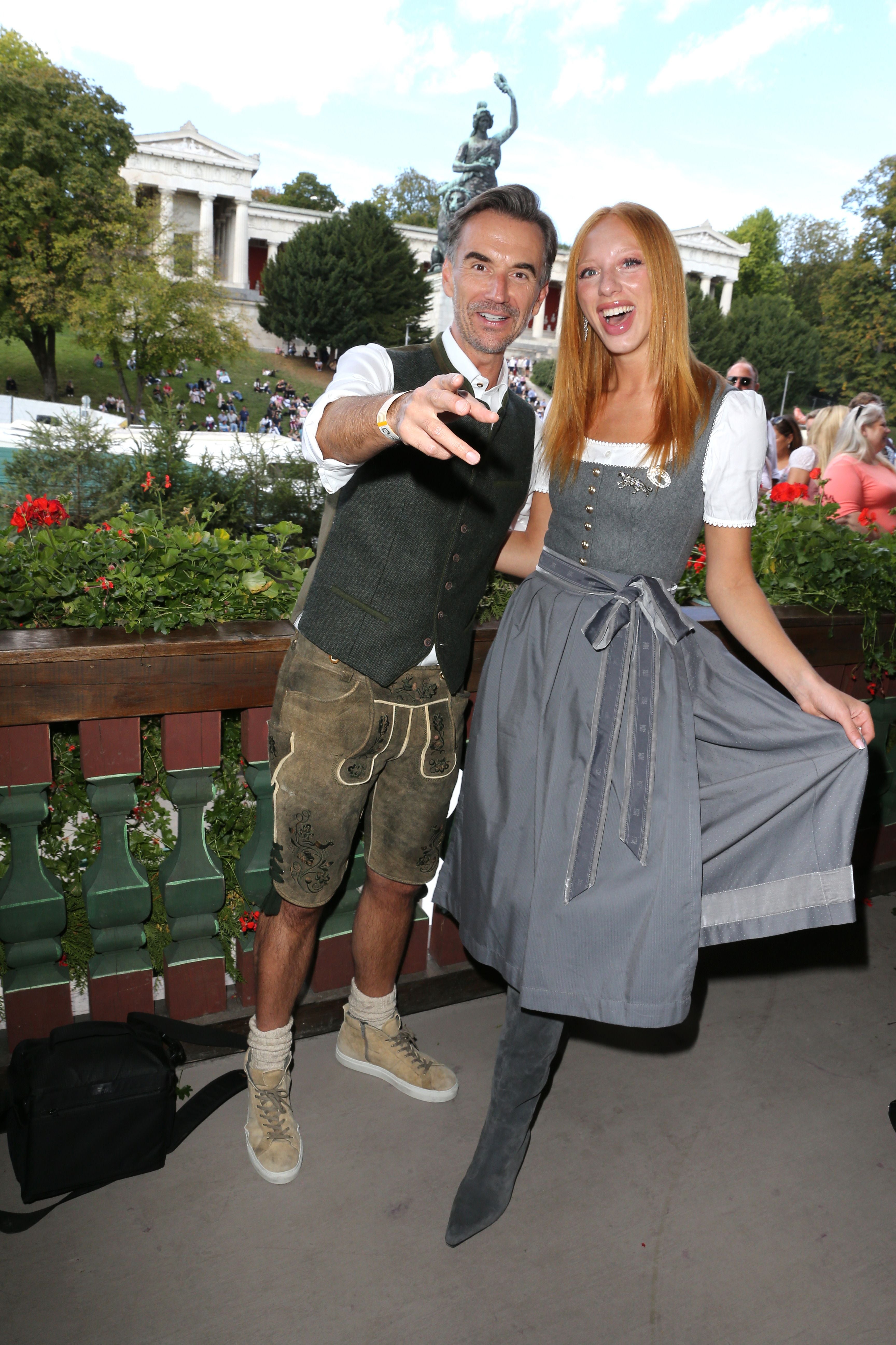 Ein Mann in Lederhose und eine Frau im Dirndl lachen gemeinsam auf dem Oktoberfest-Balkon.
