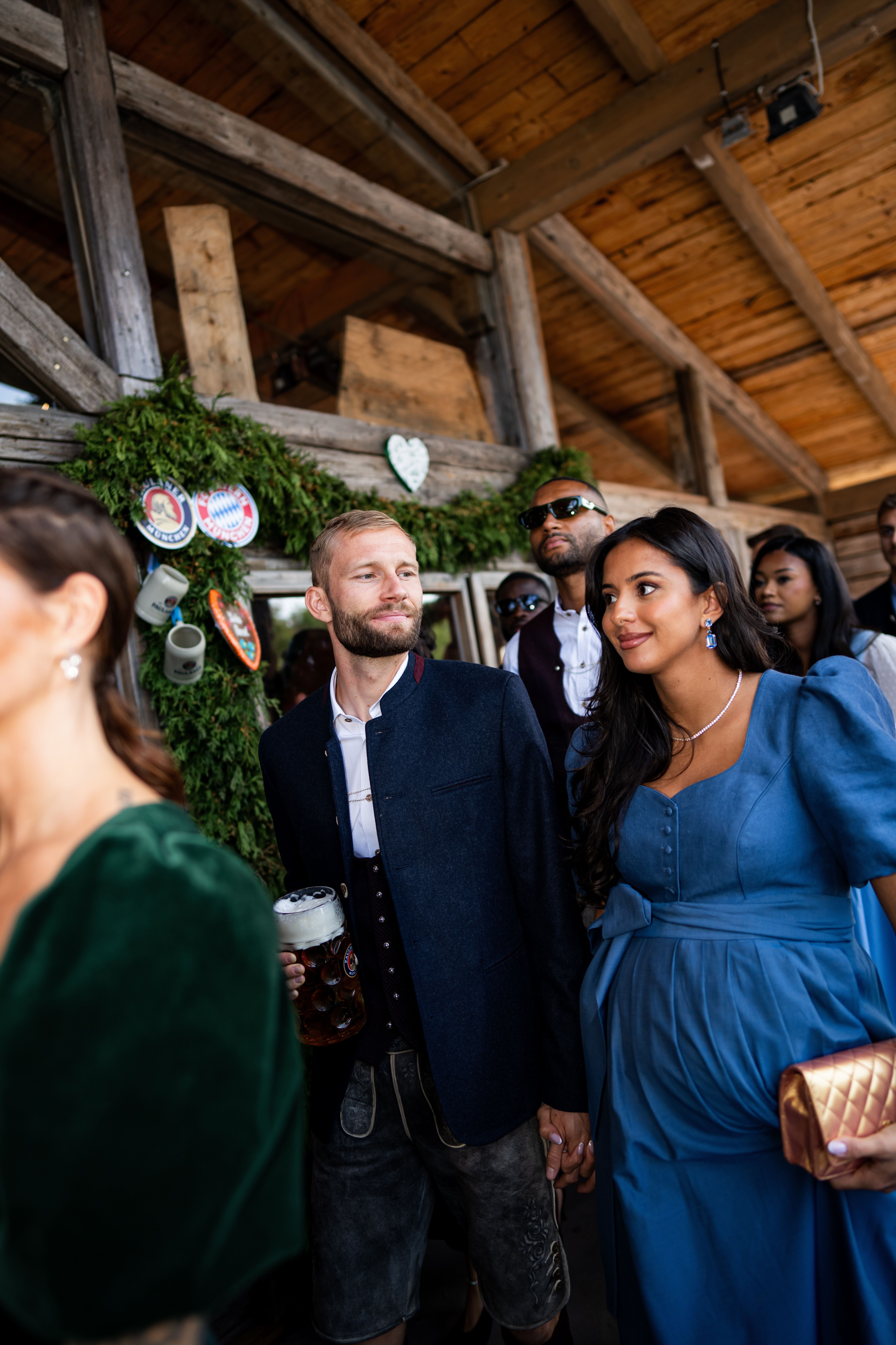 Ein Mann in Tracht hält eine Maß Bier und geht mit einer Frau im blauen Dirndl auf dem Oktoberfest.
