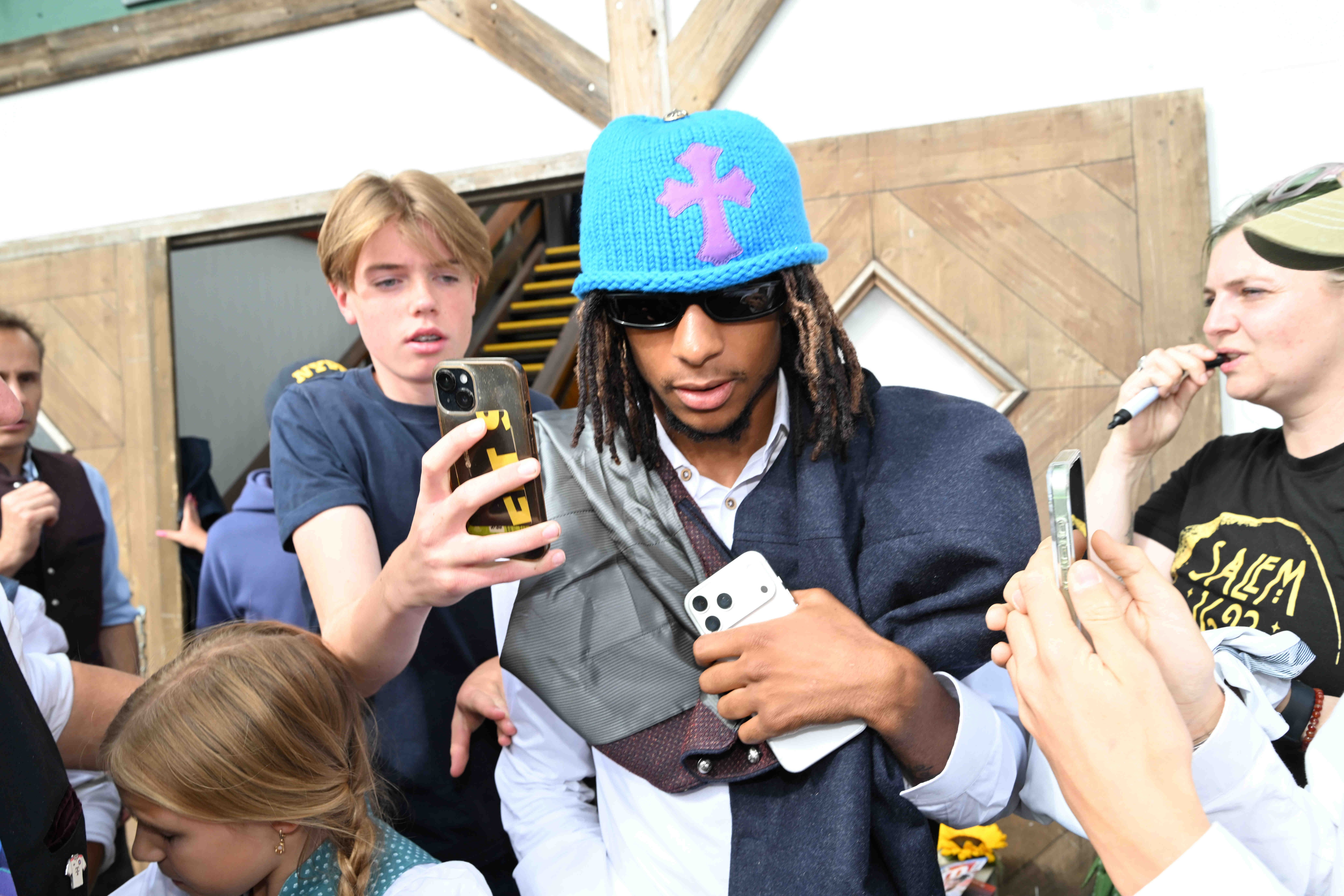 Ein Mann mit blauem Hut und Sonnenbrille wird auf dem Oktoberfest von Fans mit Handys umringt.