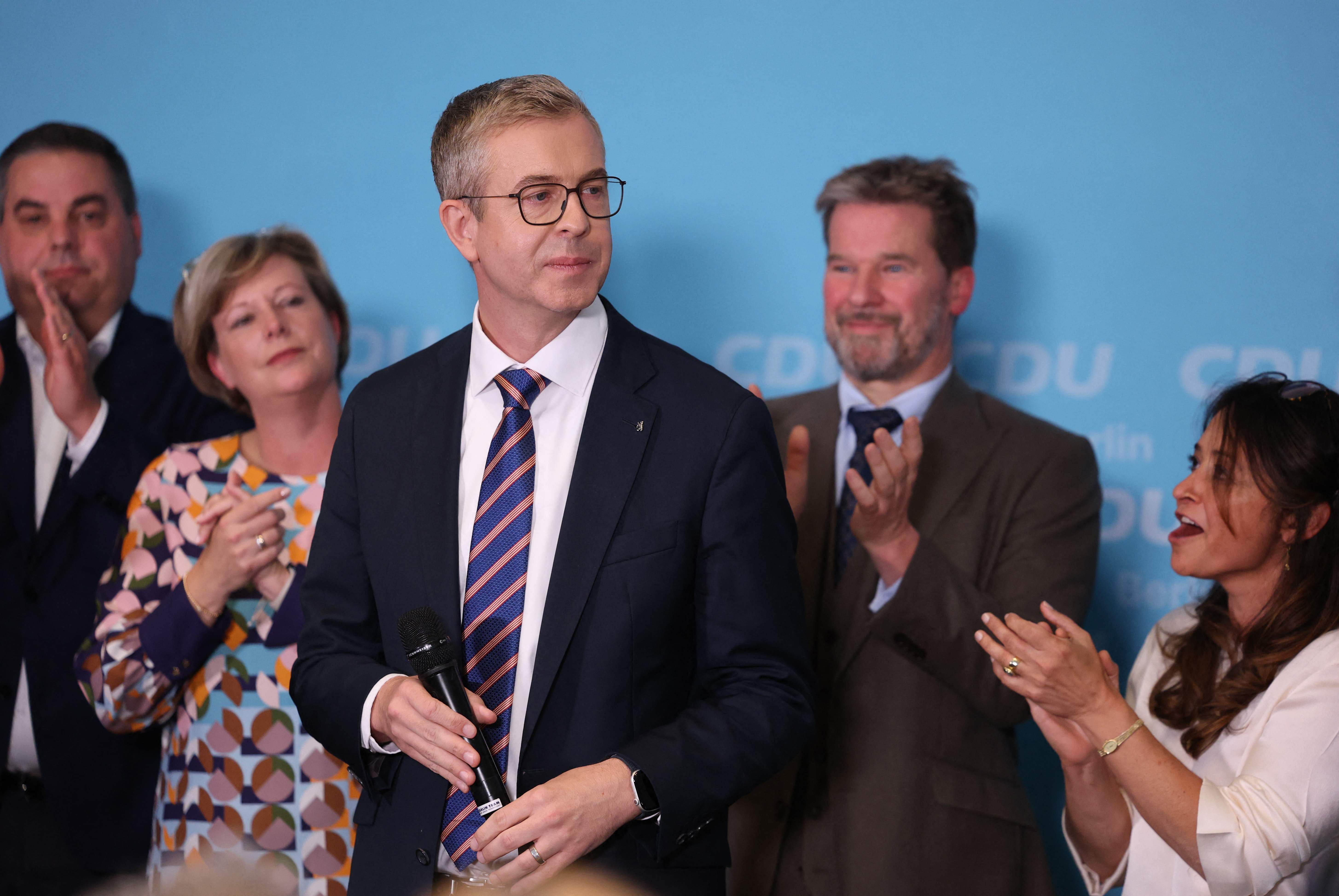 Ein Mann im Anzug hält ein Mikrofon, umgeben von applaudierenden Personen vor CDU-Logo.