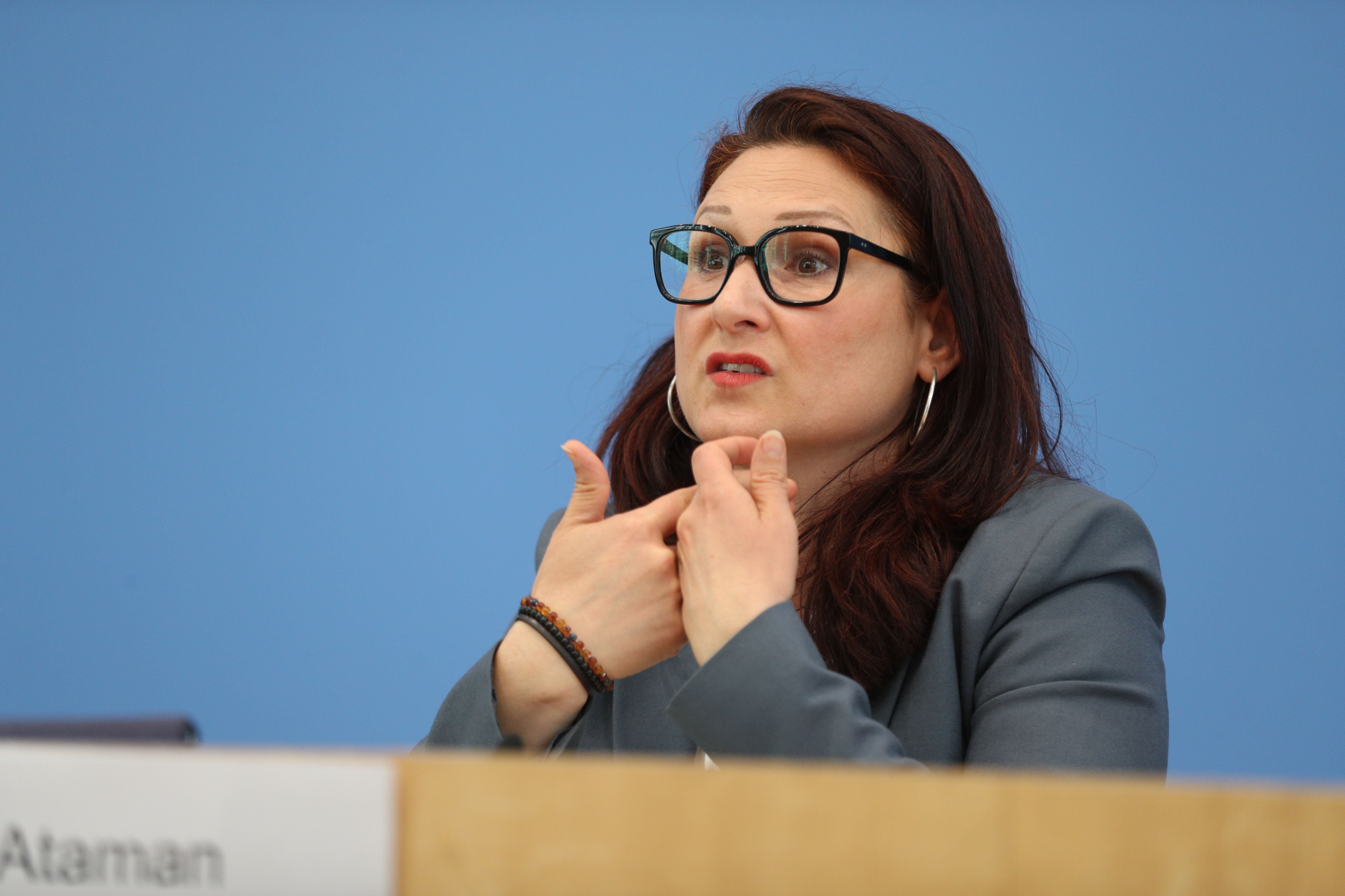 Eine Frau mit Brille spricht gestikulierend bei einer Pressekonferenz vor blauem Hintergrund.