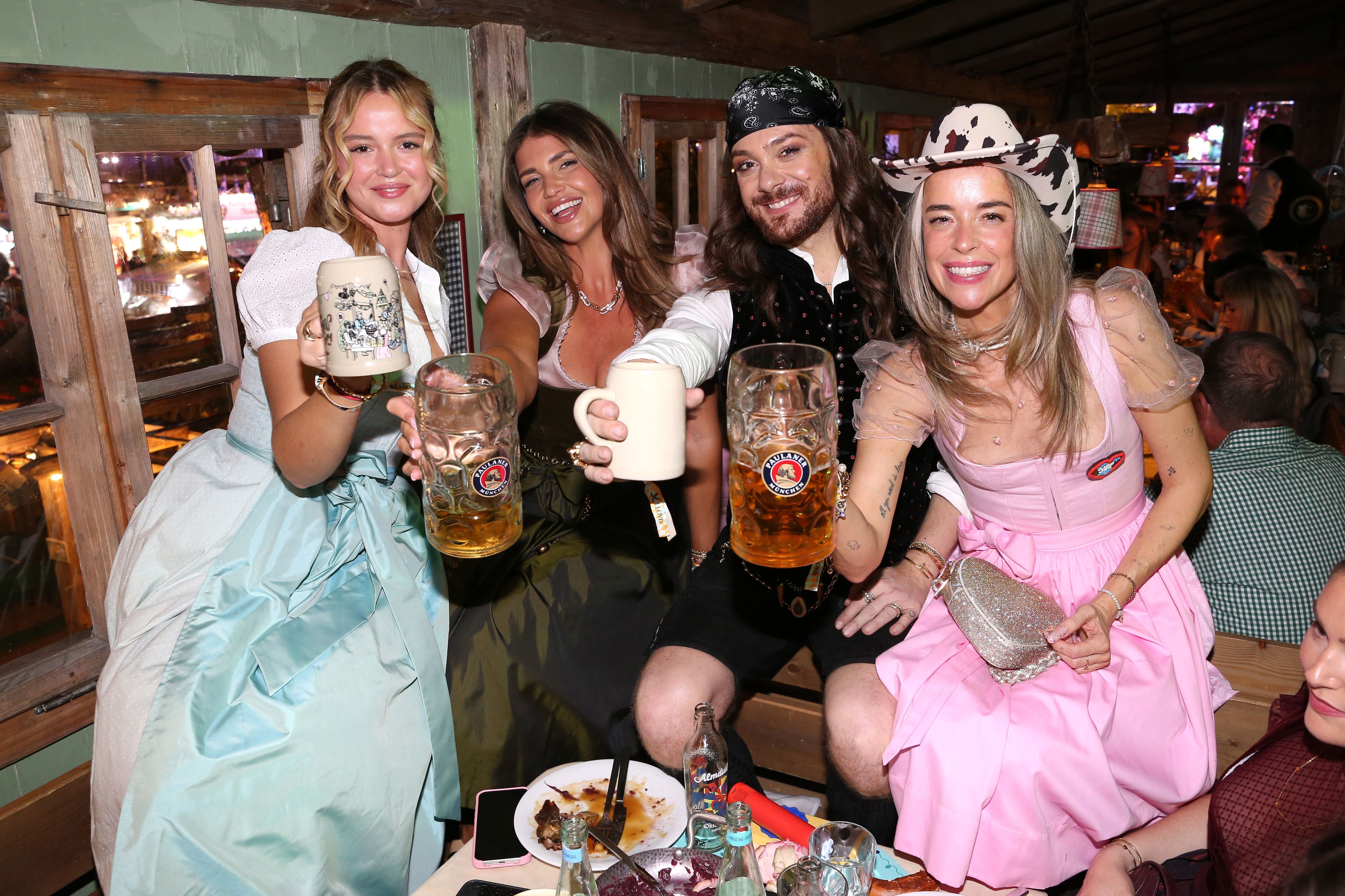 Vier fröhliche Menschen in Tracht stoßen mit Bierkrügen auf dem Oktoberfest an.