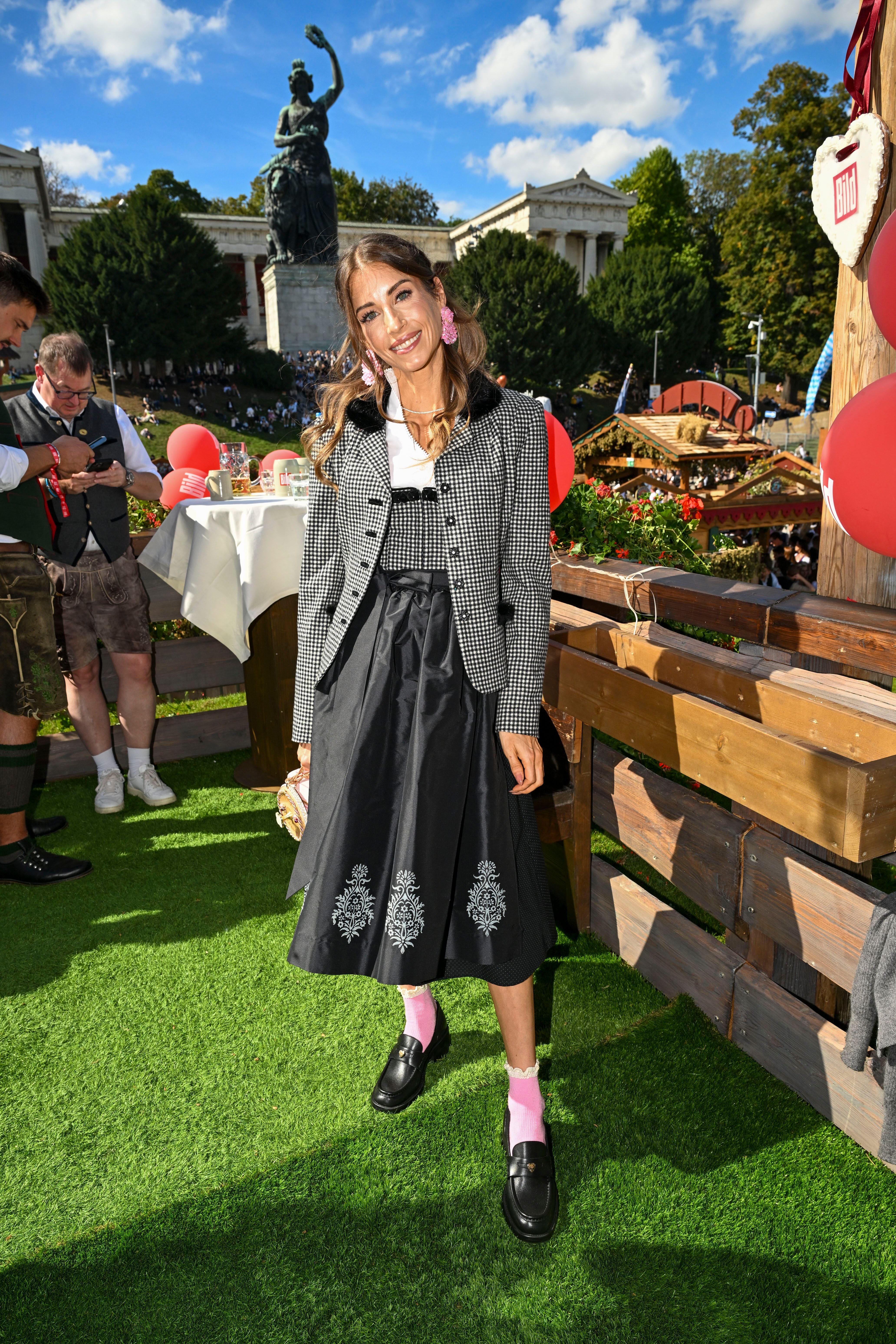 Eine Frau in Tracht steht beim Oktoberfest vor der Bavaria-Statue in München und lächelt.