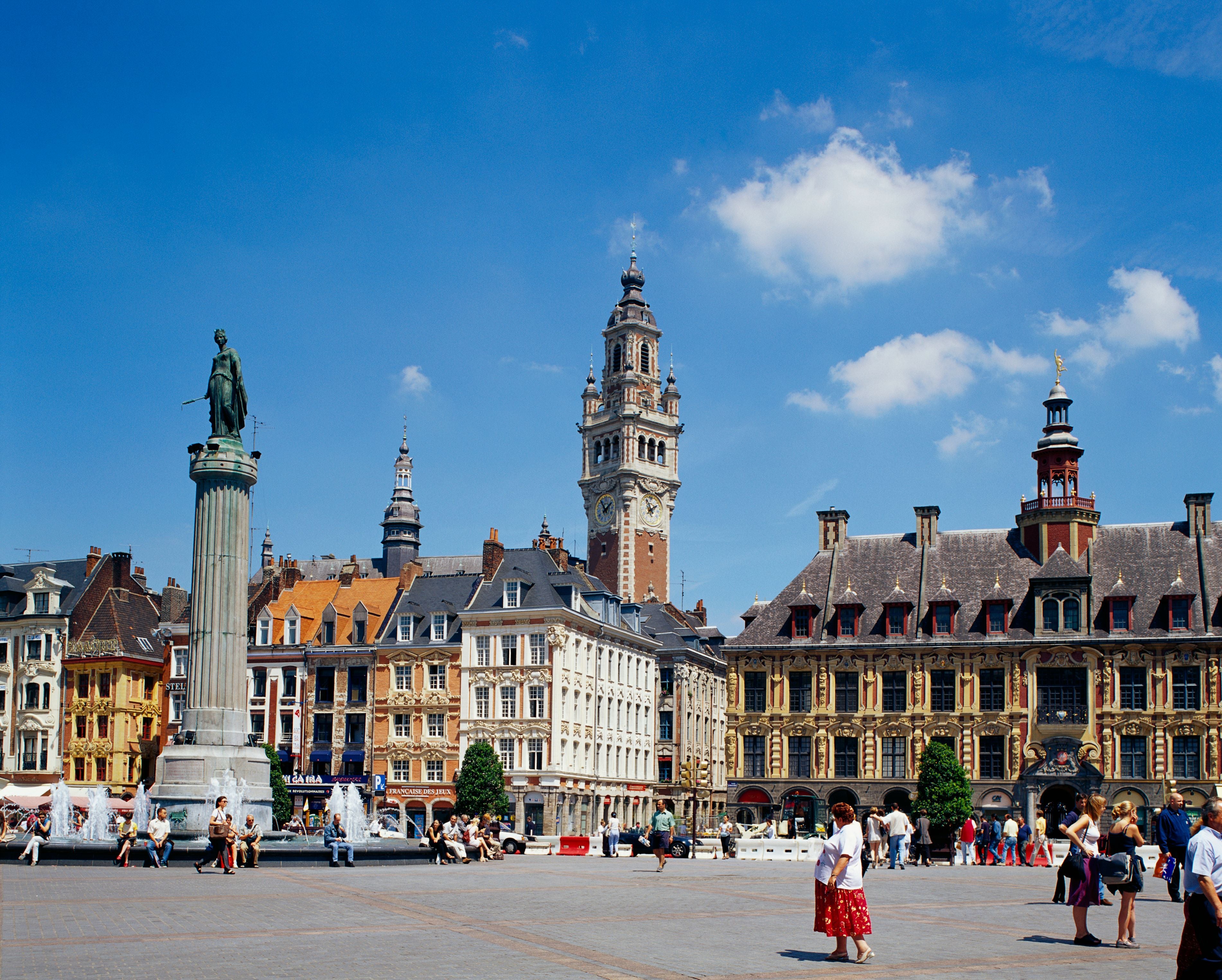 Menschen auf dem Place du Général-de-Gaulle in Lille mit historischen Gebäuden und einem Uhrturm.