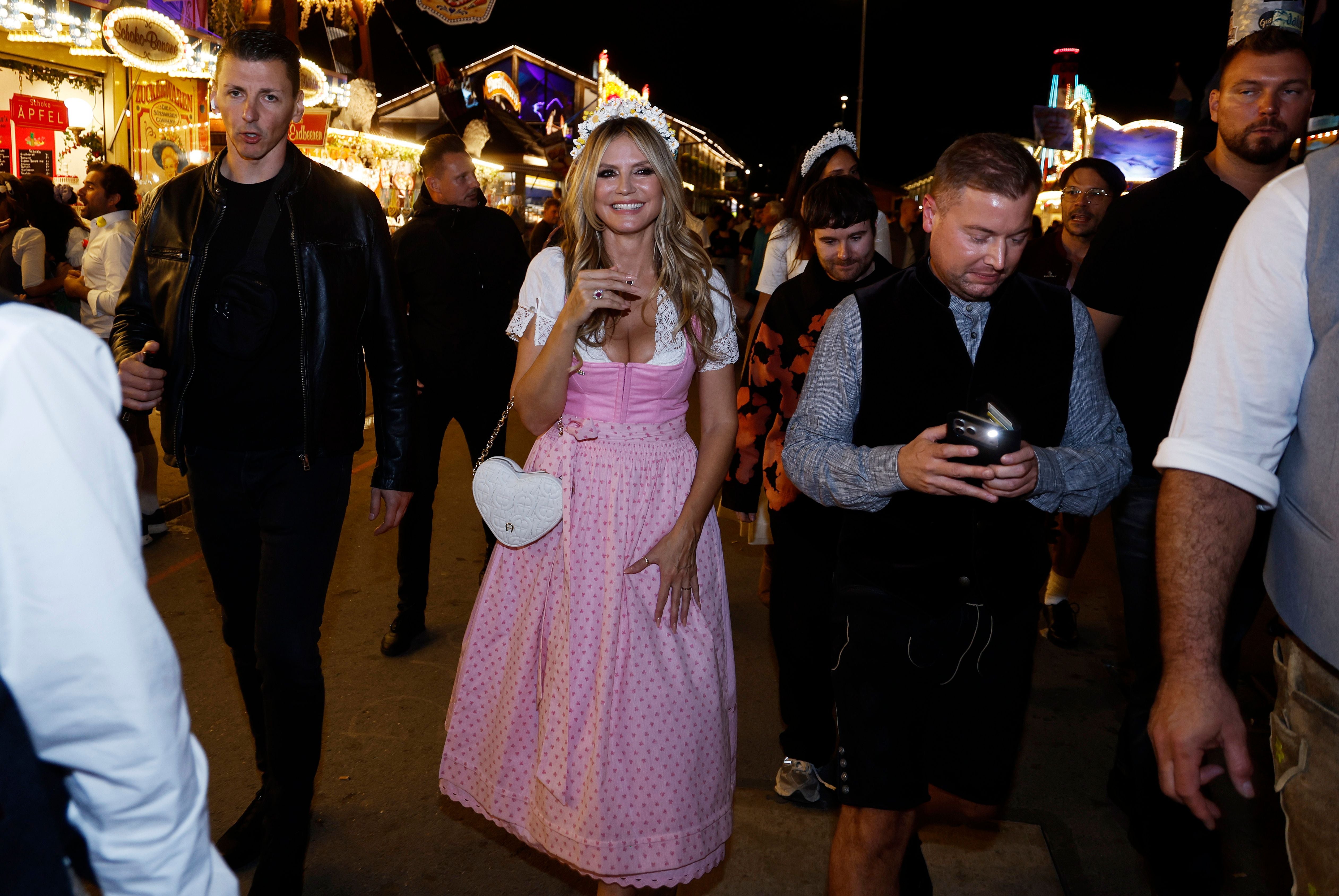 Frau in rosa Dirndl geht lachend mit einer Gruppe über das Oktoberfest-Gelände bei Nacht.